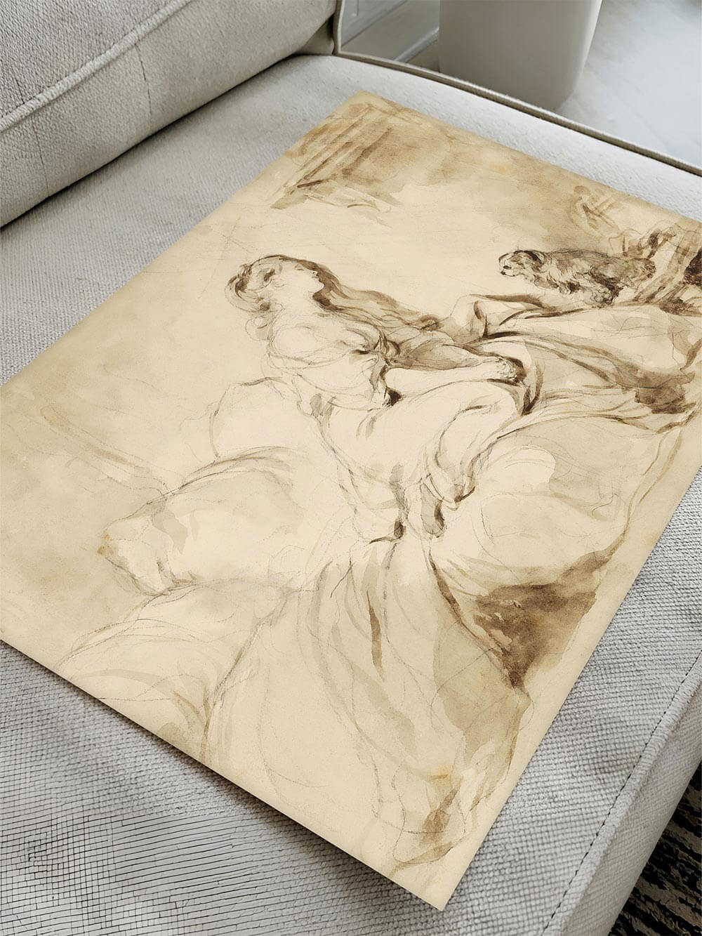Edler Rokoko-Kunstdruck in sanften Sepiatönen, der auf einem hellen Sofa liegt. Das kunstvolle Motiv einer Frau mit Hund verleiht dem Raum eine romantische und klassische Note.