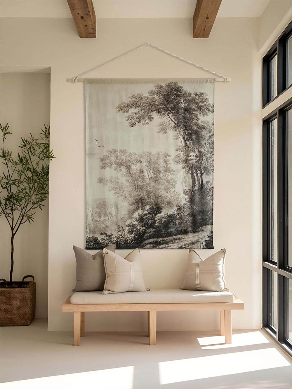 Eleganter Wandteppich mit gezeichneter Landschaft in Schwarz-Weiß. Hängt an einer cremefarbenen Wand über einer Holzbank mit neutralen Kissen. Die beruhigenden Naturszenen passen perfekt in moderne, minimalistische Räume.