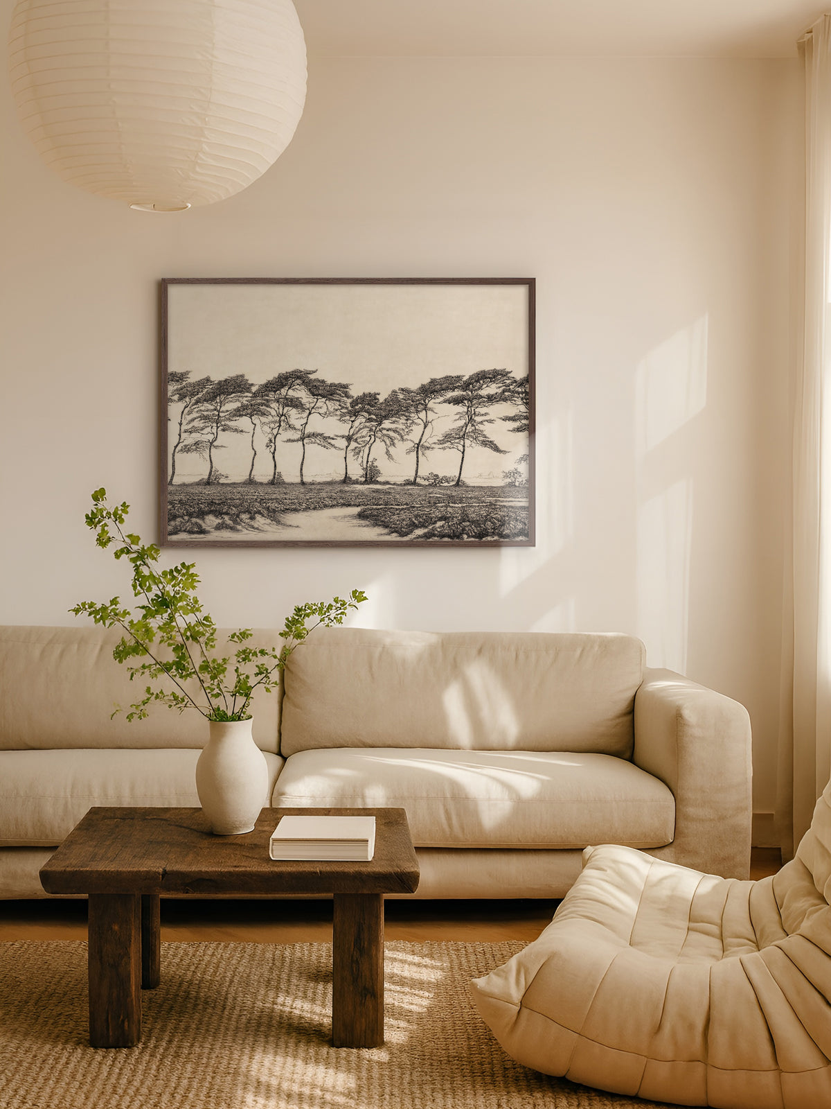 Japandi Poster mit Kiefernlandschaft im dunklen Holzrahmen über einem beigen Sofa im hellen Wohnzimmer, davor ein rustikaler Couchtisch mit weißer Vase und Zweigen unter einer Papierlampe. Die feine Zeichnung passt zu den warmen Naturtönen des Raums.
