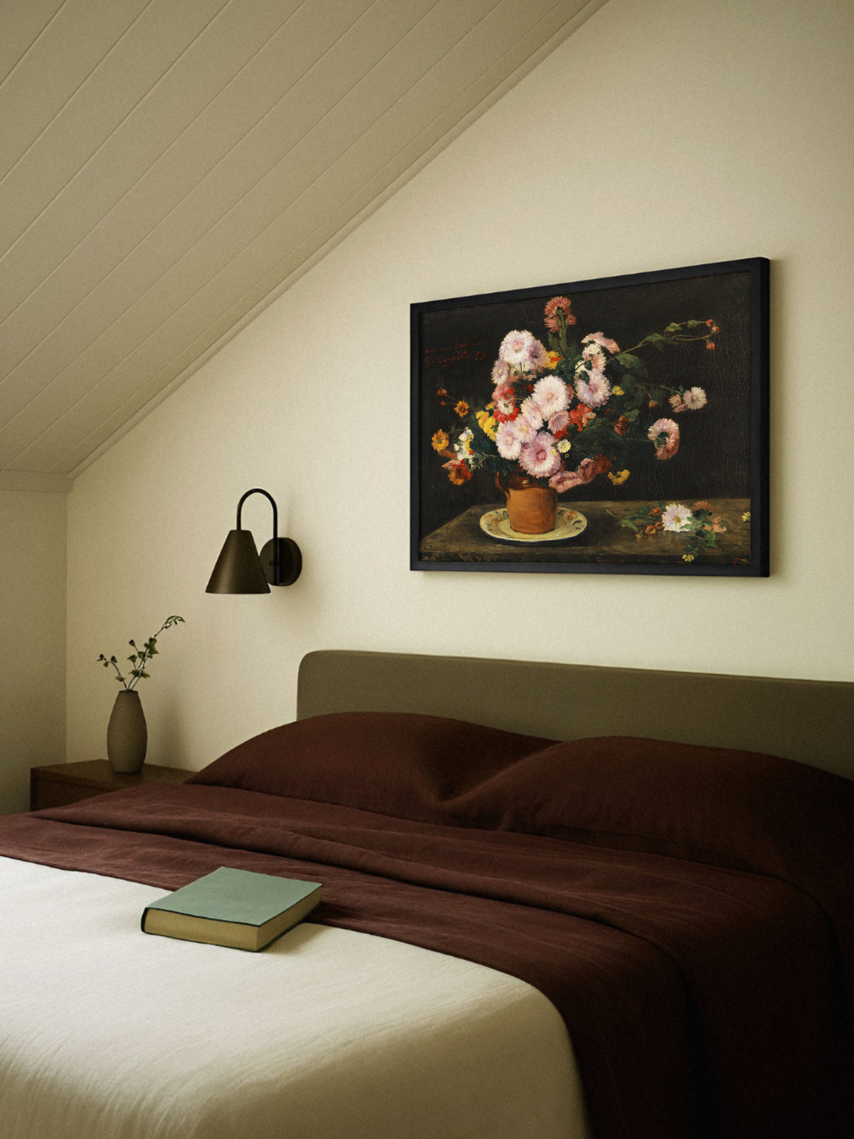 Blumen Poster mit Astern im schwarzen Rahmen über einem Bett mit bordeauxroter Bettwäsche und olivgrünem Kopfteil unter einer Dachschräge, daneben eine Wandleuchte und eine Vase mit Zweig. Das dunkle Stillleben passt zu einem warmen, moody Schlafzimmer.