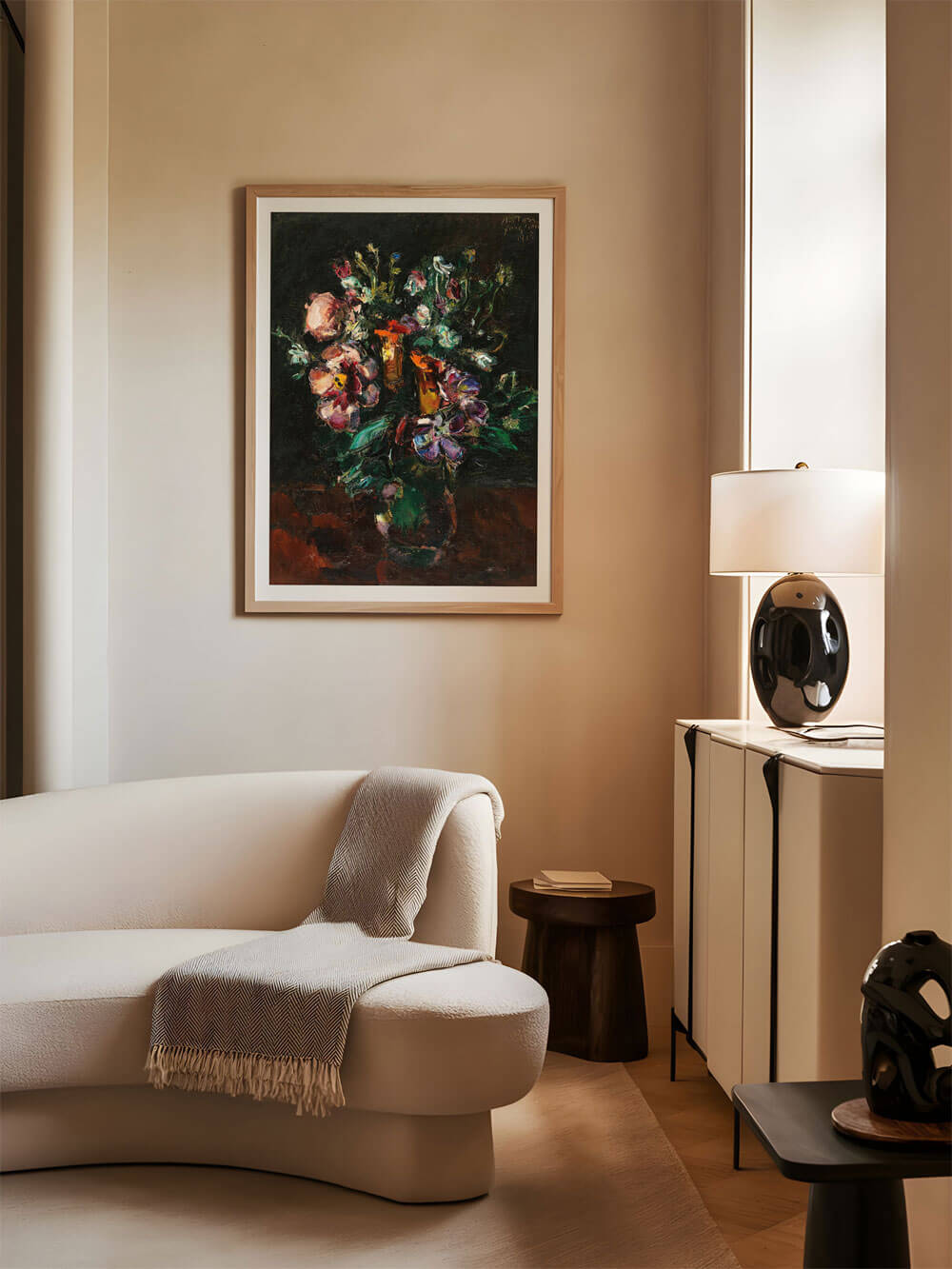 Ein modernes Wohnzimmer mit neutralen Farben und einem weichen cremefarbenen Sofa. An der Wand hängt ein dunkles, impressionistisches Gemälde eines Blumenarrangements. Die kräftigen, farbigen Blüten des Bildes heben sich intensiv vom dunklen Hintergrund ab und schaffen eine kontrastreiche und stimmungsvolle Atmosphäre.