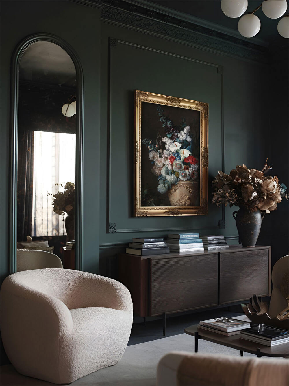 Ein Blumenstillleben im prunkvollen goldenen Rahmen, hängt in einem eleganten, dunkelgrün gestrichenen Wohnzimmer. Es wird durch eine gemütliche cremefarbene Lounge mit einem modernen Design betont. Der Raum vermittelt ein Gefühl von Opulenz und Ruhe mit warmem, indirektem Licht.
