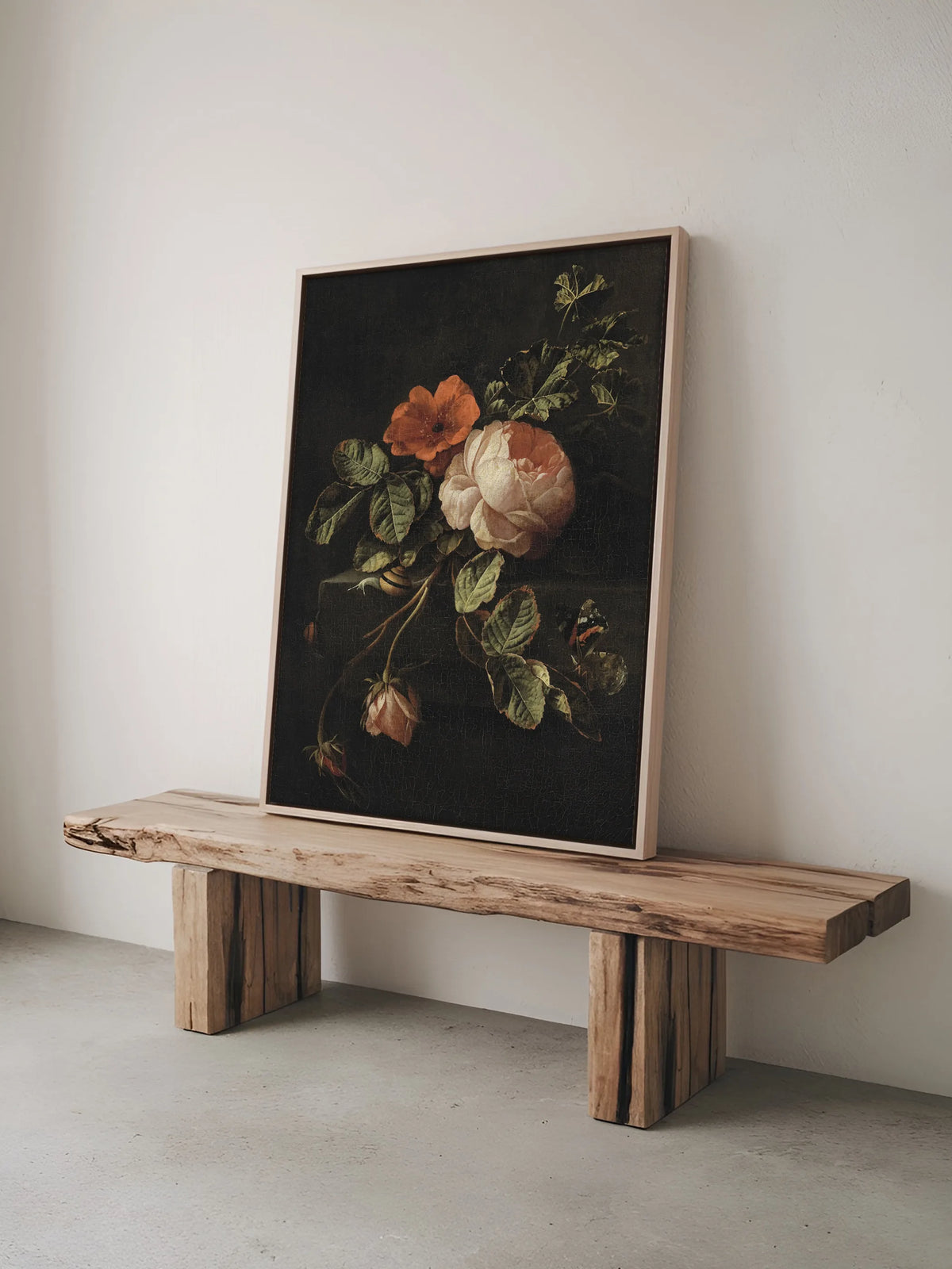 Leinwandbild mit Rosenstillleben im Naturholzrahmen lehnt auf einer rustikalen Bank aus Massivholz vor einer hellen Wand. Das barocke Wandbild wirkt vor dem rohen Holz besonders warm.