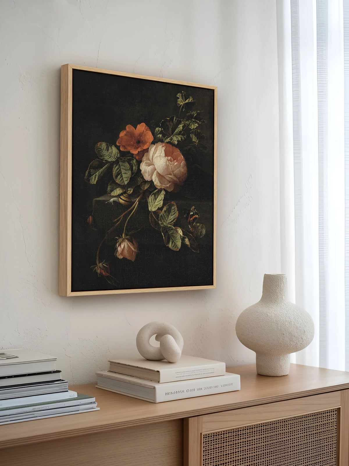 Leinwandbild mit Rosenstillleben im Naturholzrahmen über einem Sideboard mit Rattanfront, Büchern und Keramikvase. Das dunkle barocke Wandbild bildet einen Gegenpol zur hellen Japandi Einrichtung.