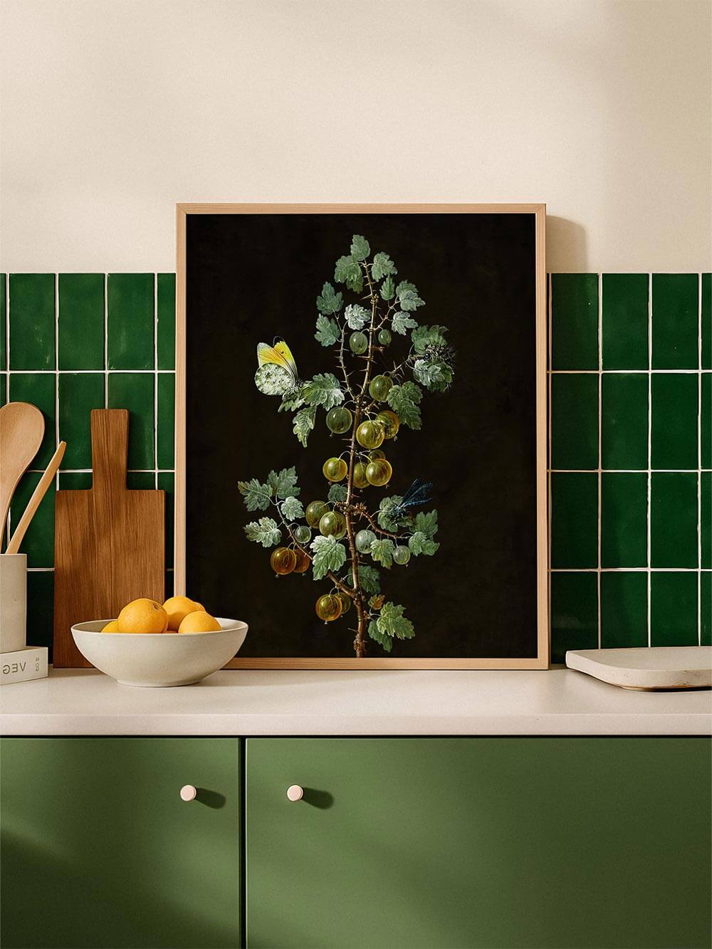 Der Vintage-Kunstdruck mit Stachelbeeren steht gerahmt auf einer weißen Küchenzeile vor grünen Fliesen. Die botanische Illustration bringt Ruhe und Tiefe in den Raum.
