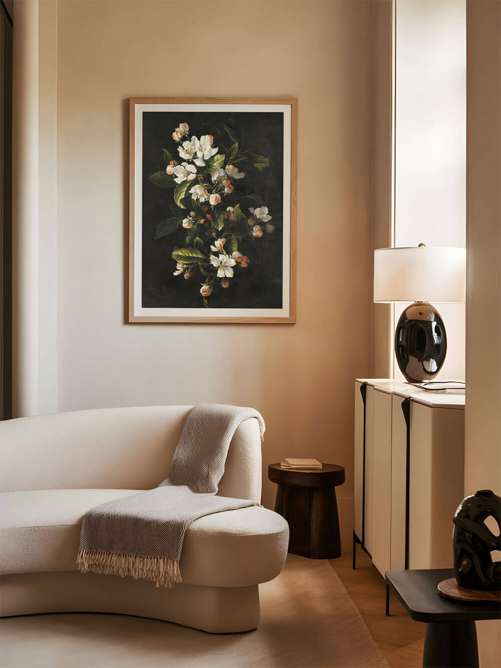 Ein Kunstdruck mit weißen Blüten auf einem dunklen Hintergrund ist in einem modernen, neutral eingerichteten Wohnzimmer zu sehen. Die Blüten sind fein ausgearbeitet und stehen im Kontrast zu den weichen Beigetönen der Einrichtung. Das Bild verleiht dem Raum eine elegante und ruhige Atmosphäre.