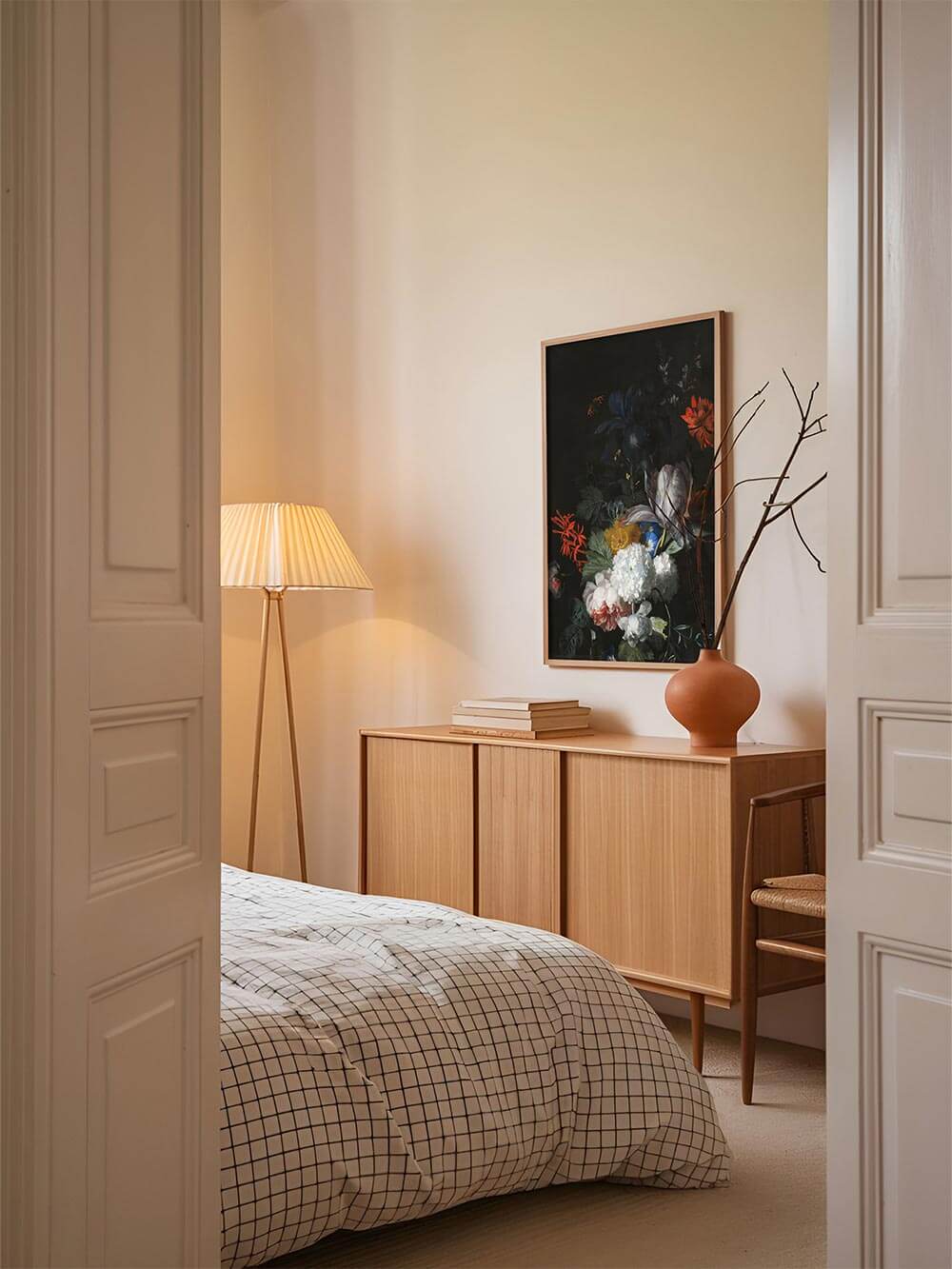Dunkler Blumen Kunstdruck hängt gerahmt über einem Holzschrank im Schlafzimmer. Die barocke Blumen Kunst schafft eine ruhige, zugleich dramatische Atmosphäre.
