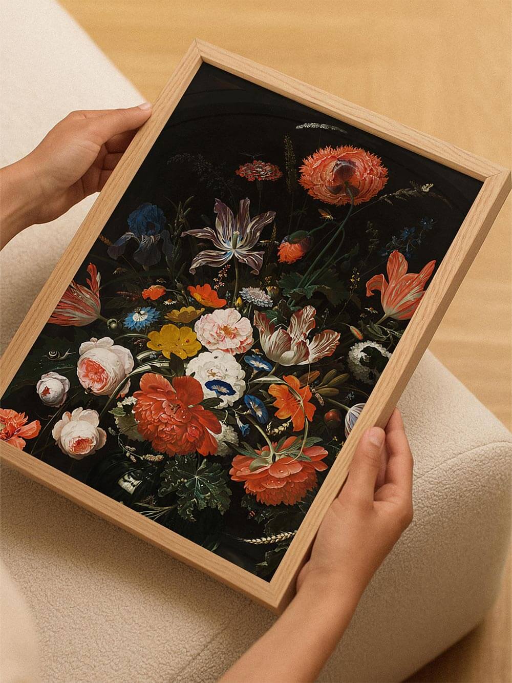 Eine Person hält einen barocken Blumen-Kunstdruck im Holzrahmen. Die farbintensiven Blüten leuchten vor dem dunklen Hintergrund und entfalten ihre elegante Wirkung.