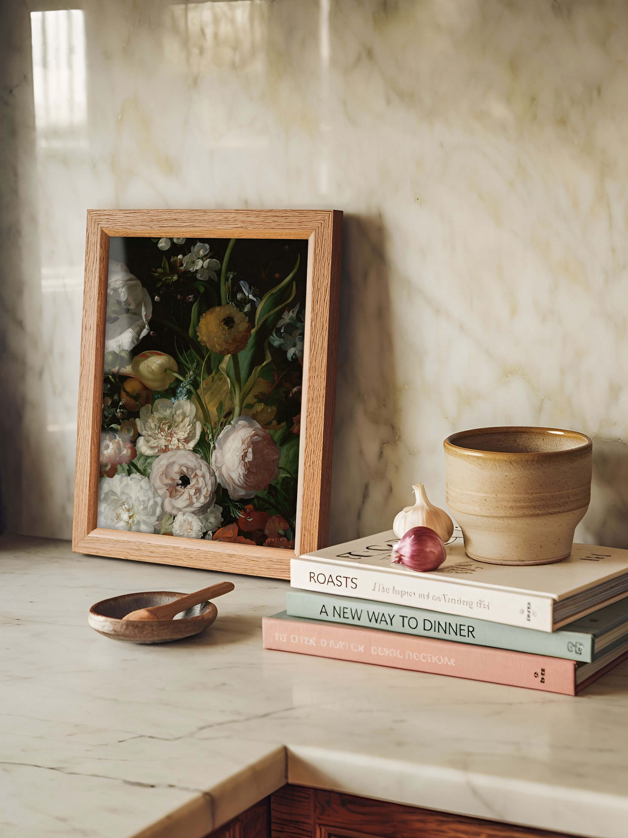Gerahmter Kunstdruck mit barockem Blumenstillleben lehnt auf einer Marmorarbeitsplatte neben Kochbüchern, Knoblauch und einer Keramikschale. Der Holzrahmen und die gedämpfte Farbpalette setzen einen ruhigen Akzent in der hellen Küche.