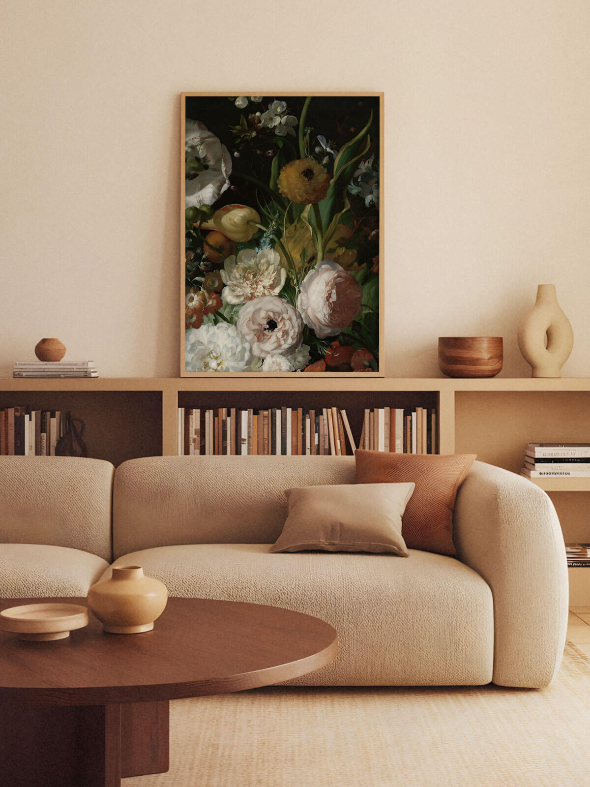 Hell gerahmter Kunstdruck mit barockem Blumenstillleben hängt über einem niedrigen Bücherregal hinter einem beigen Sofa. Das dunkle, gedämpft-warme Motiv fügt sich harmonisch in die erdtonige Wohnzimmergestaltung ein.