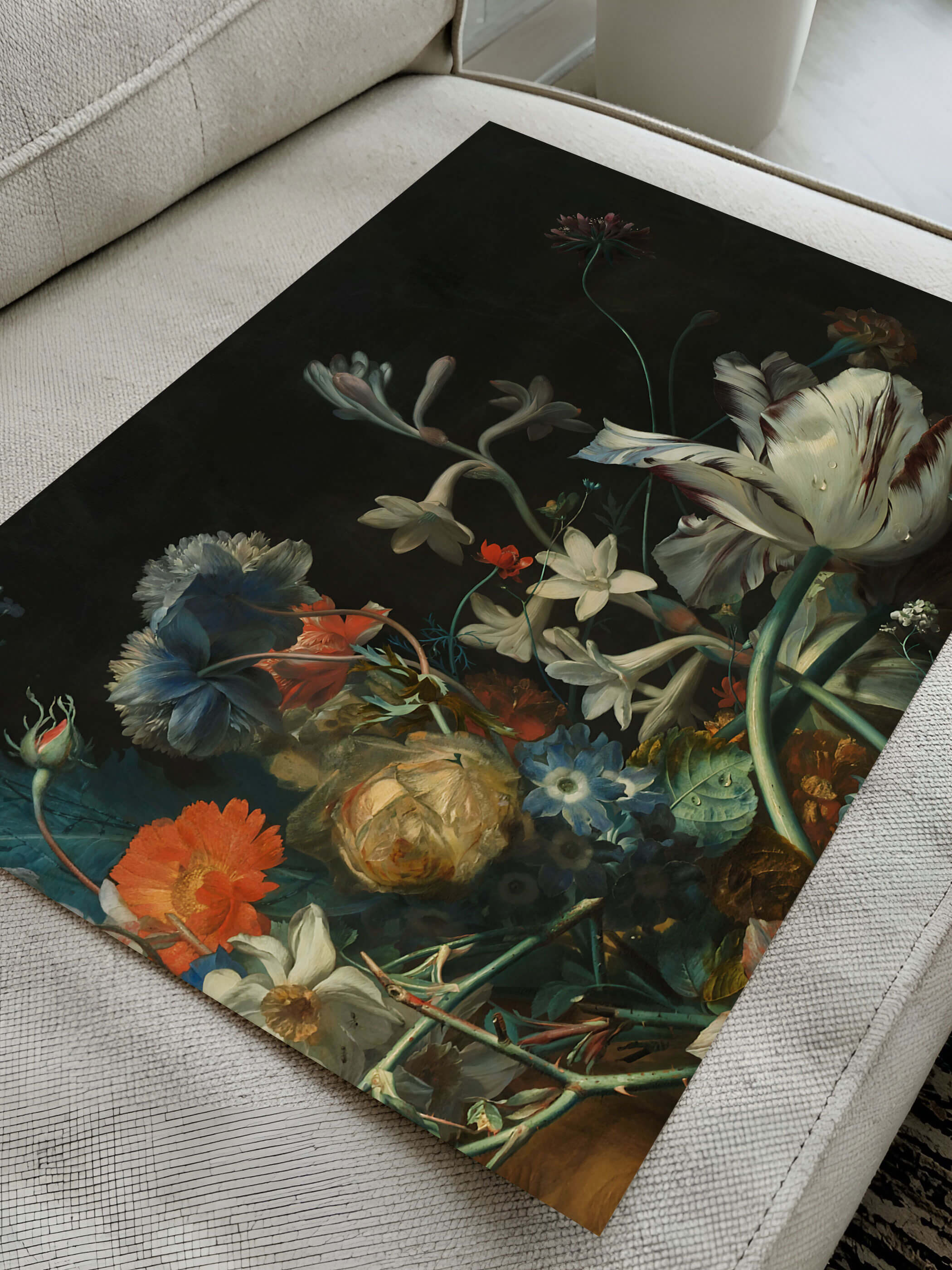 Kunstdruck mit barockem Blumenstillleben aus Tulpe, Narzissen und blauer Nelke liegt diagonal auf einem cremefarbenen Sofa. Die Nahaufnahme zeigt die Papierqualität und die feinen Farbnuancen des Motivs im Detail.