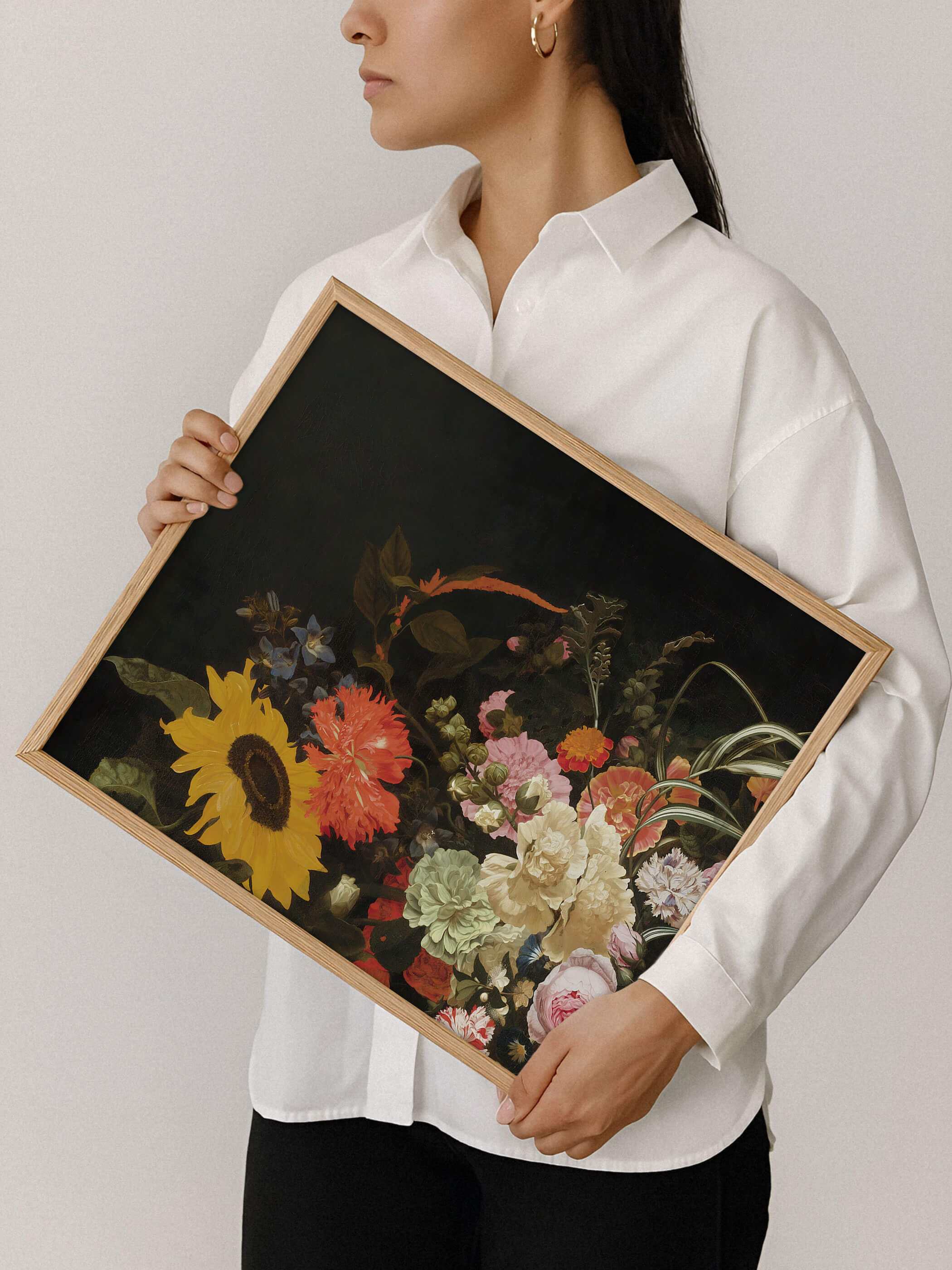 Eine Frau in weißem Hemd hält einen Holzrahmen mit dem barocken Blumenstillleben aus Sonnenblume und Nelken vor neutralem Hintergrund. Der Kunstdruck zeigt die kräftigen Farben und die feine Rahmung im Detail.