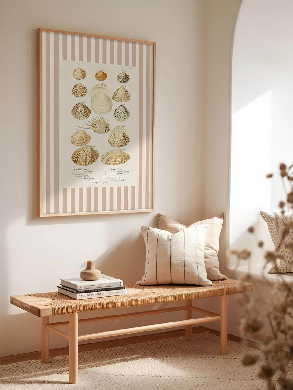 Künstlerisch illustrierter Muschel-Druck im botanischen Stil, eingerahmt von roséfarbenen Streifen, hängt in einem hellen Flur über einer Holzbank mit Kissen. Dezente Farben erzeugen mediterranes Flair.

