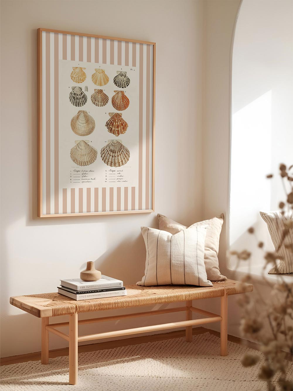 Heller Flur mit Muschel-Kunstdruck mit Streifenmuster  an cremefarbener Wand, dekoriert mit Kissen, Büchern und Naturmaterialien – harmonische Wanddekoration im Küstenstil.