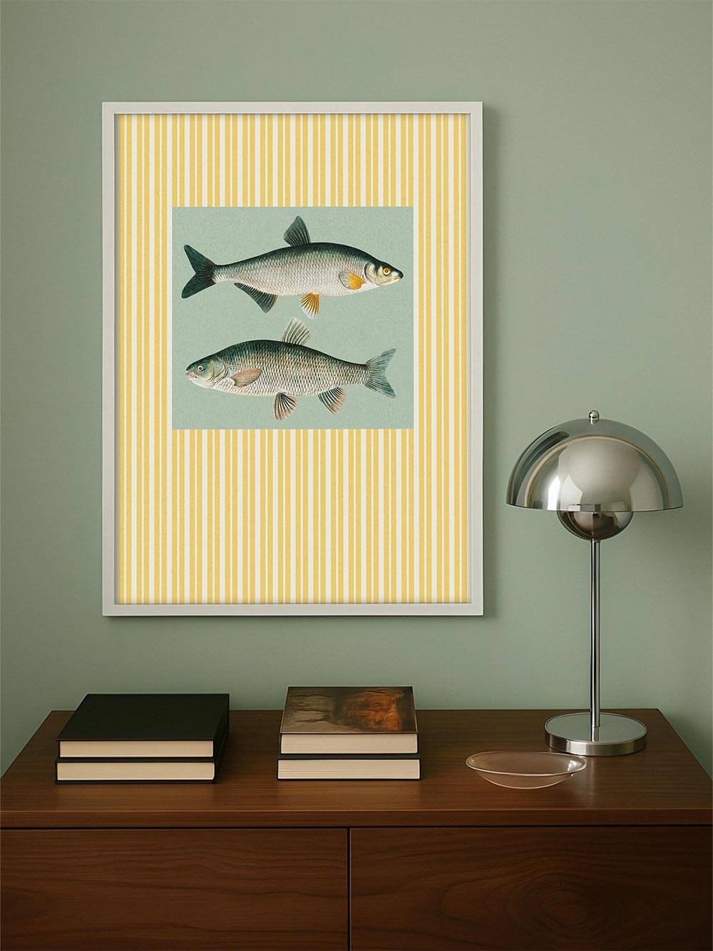 Der Fisch-Kunstdruck hängt über einem Mid-Century-Sideboard mit Büchern und Metalllampe. Das Streifenmuster bringt grafische Klarheit in den Raum.