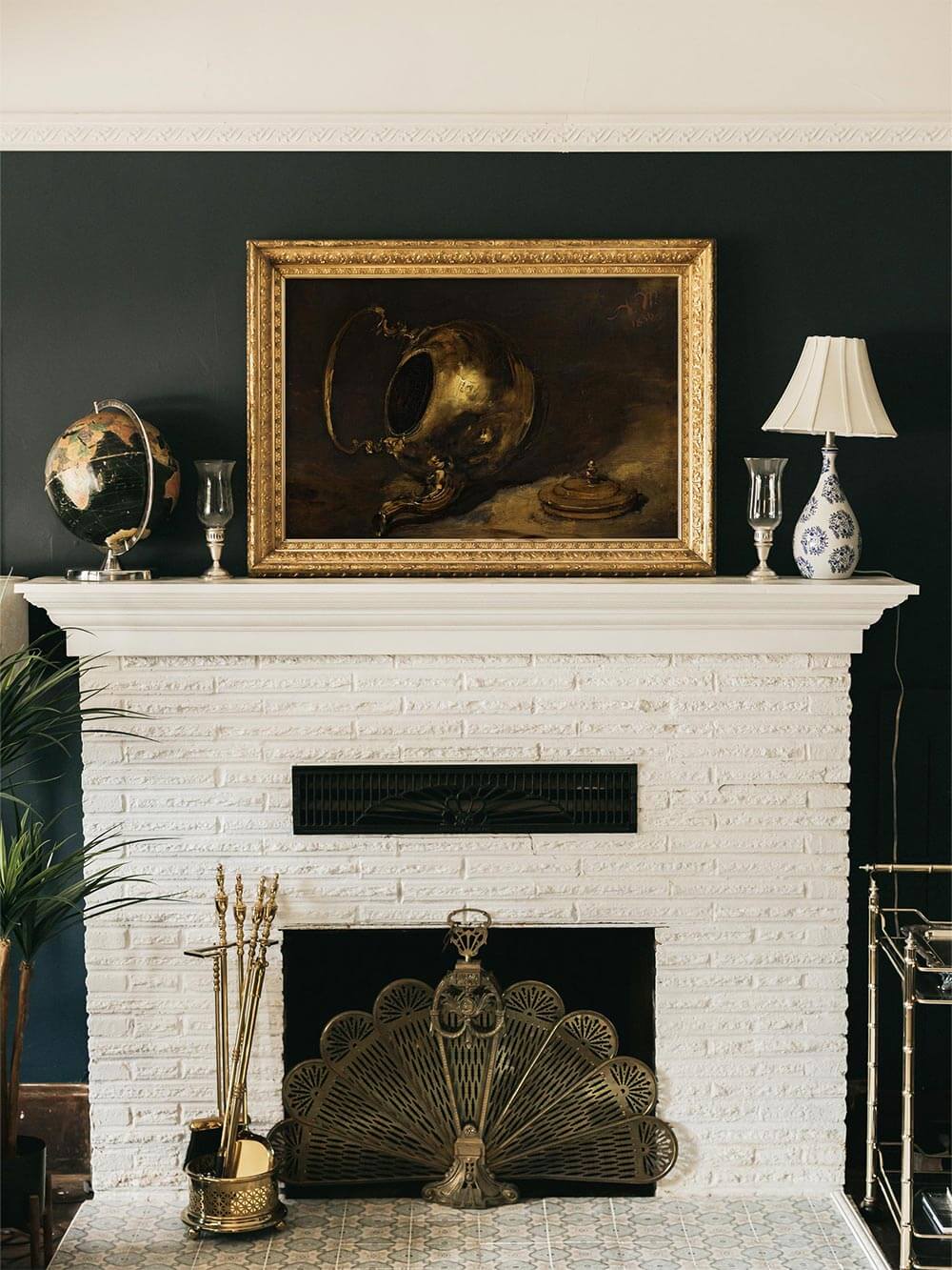 Eleganter Kunstdruck mit goldener Teekanne im prunkvollen Rahmen über weißem Kamin. Dunkle Farbpalette und Realismus erzeugen historische, wohnliche Tiefe.