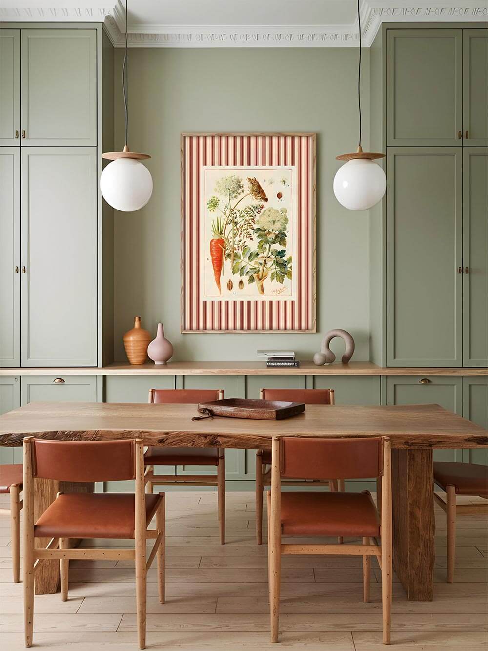 Stilvoll inszenierter Kunstdruck mit botanischem Motiv, gerahmt von rot-beigen Streifen, als Blickfang an olivgrüner Wand im Esszimmer mit Holz- und Lederakzenten im natürlichen Japandi-Stil.