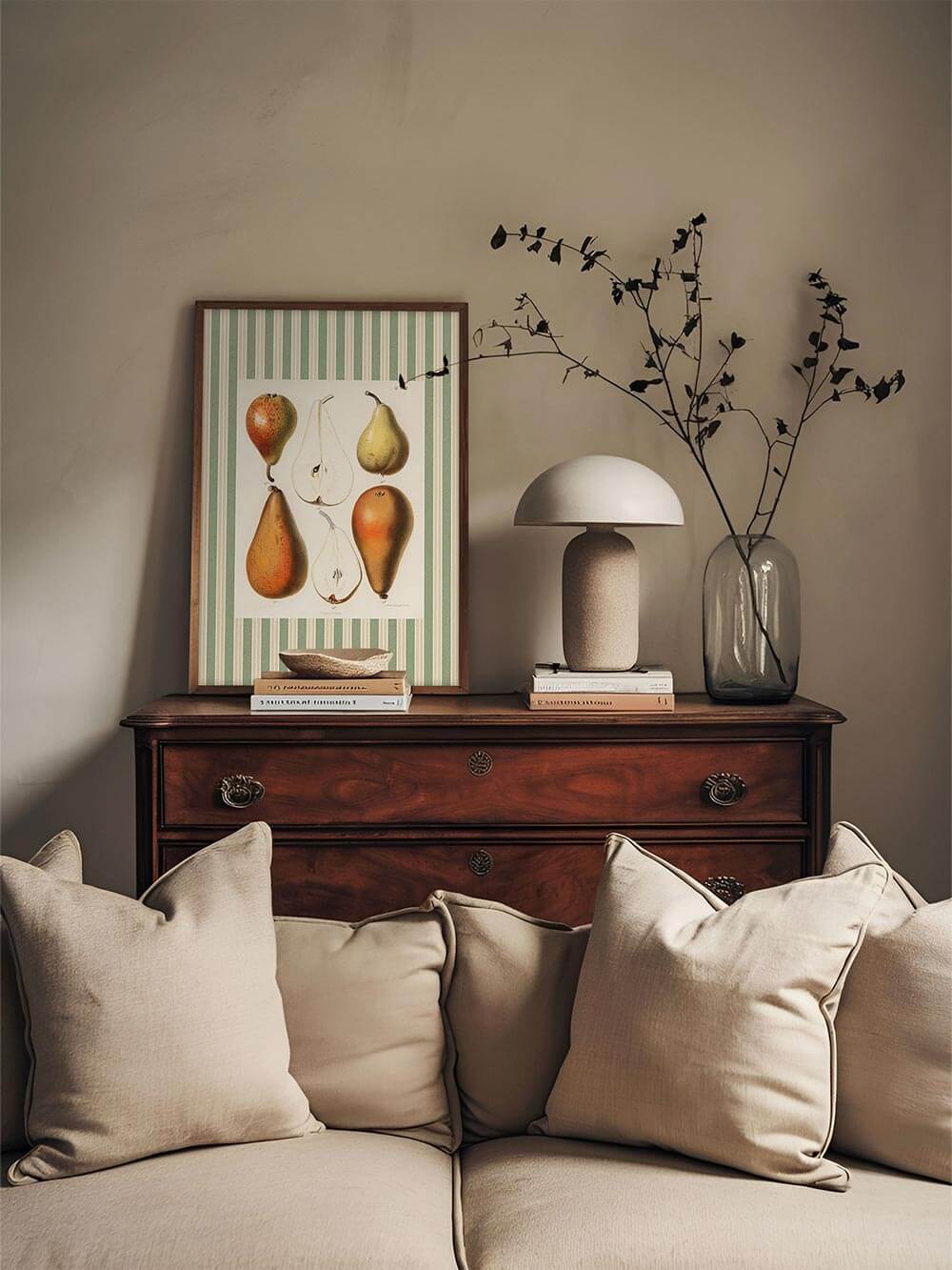 Vintage Birnen-Kunstdruck auf einer antiken Holzkommode, kombiniert mit minimalistischer Deko und neutralem Sofahintergrund für eine warme, nostalgische Raumwirkung.