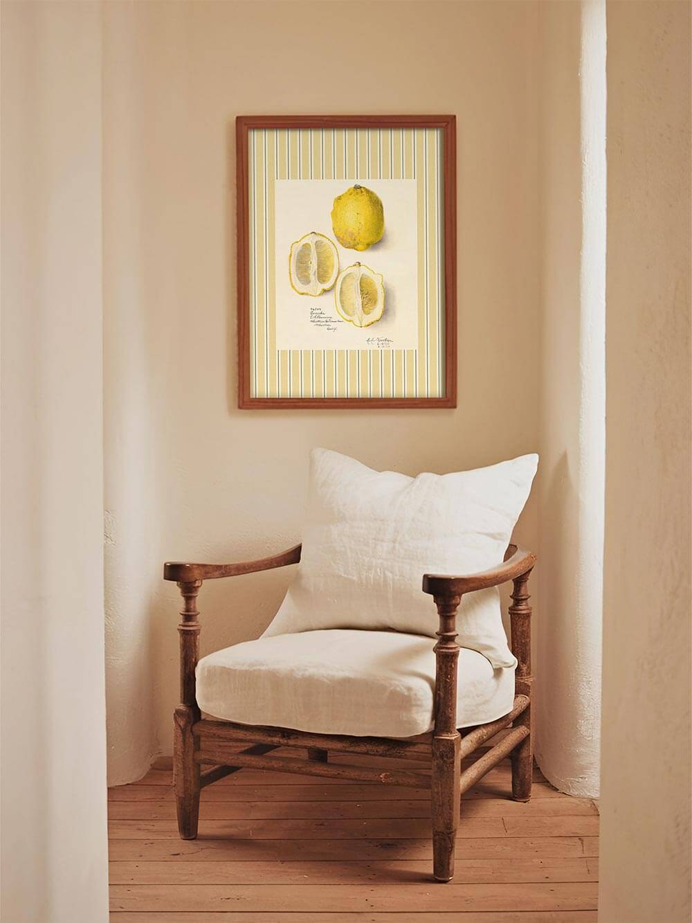 Botanisches Zitronenbild mit gelb gestreiftem Rahmen als warmer Farbakzent über einem rustikalen Sessel im mediterranen Interieur mit natürlichem Licht.