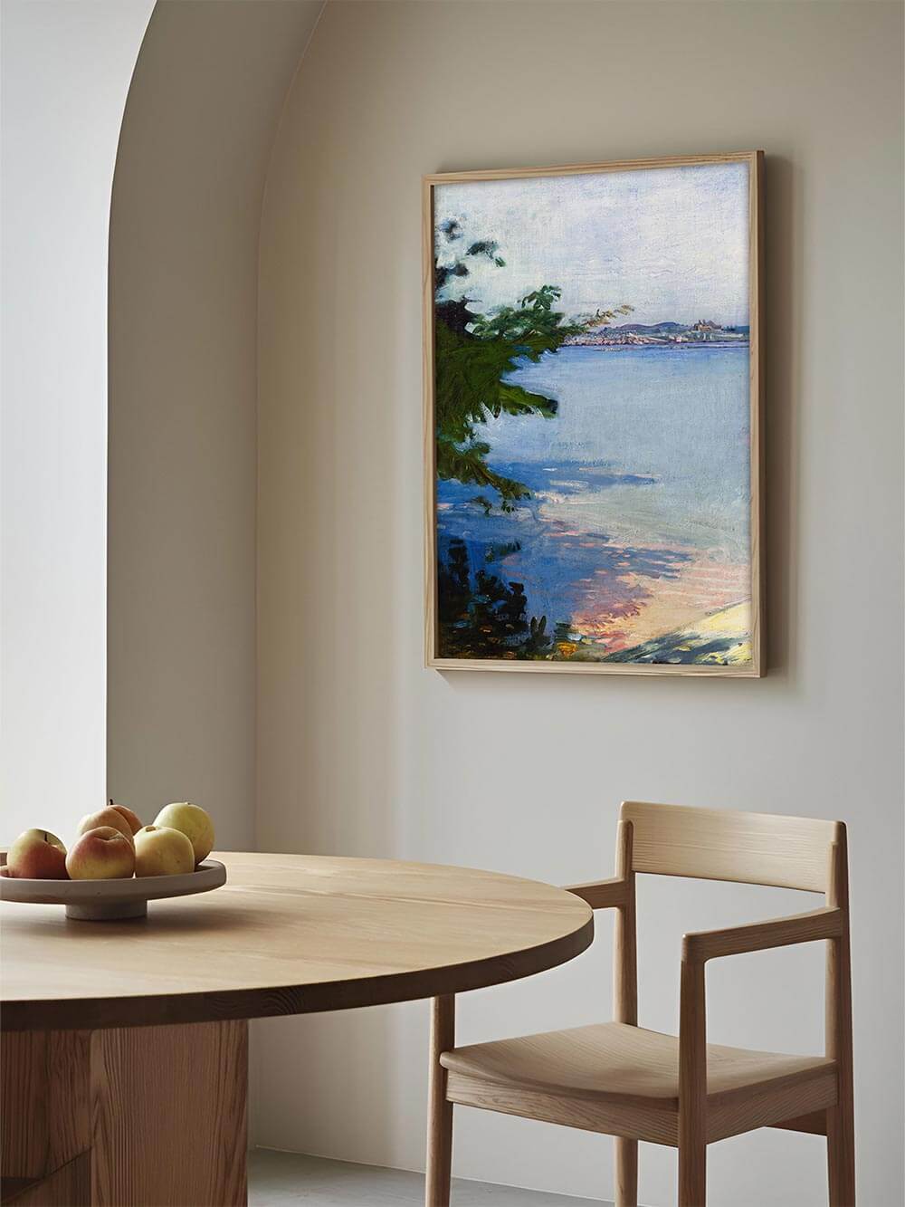 Kunstdruck einer impressionistischen Seenlandschaft mit sanften Blautönen und grünen Akzenten, gerahmt an einer beigen Wand über einem runden Holztisch im Esszimmer – stilvolle Wandkunst für ein natürliches Interieur.