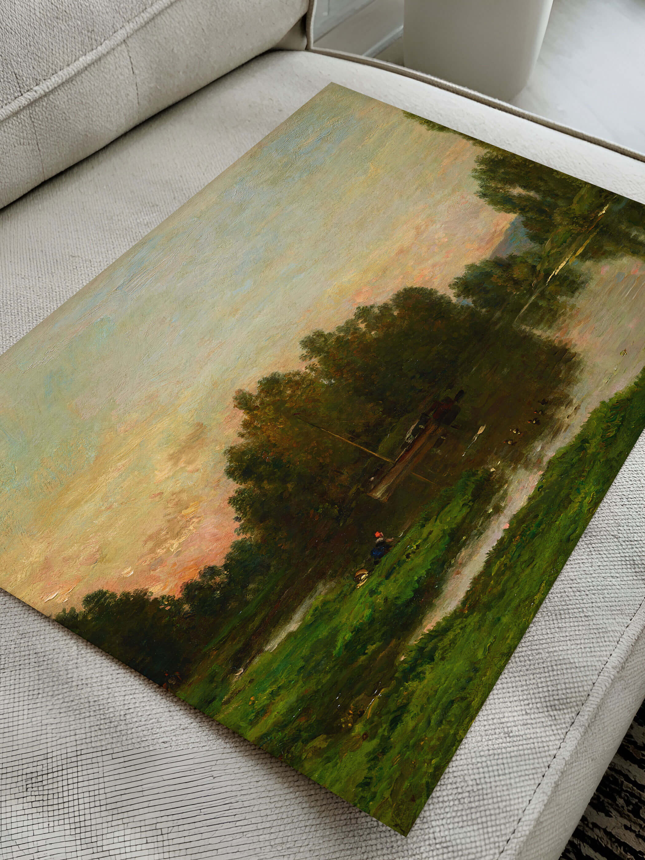 Nahaufnahme eines Landschaftsposters mit idyllischem Fluss und grünem Ufer, das auf einem hellgrauen Sofa liegt.