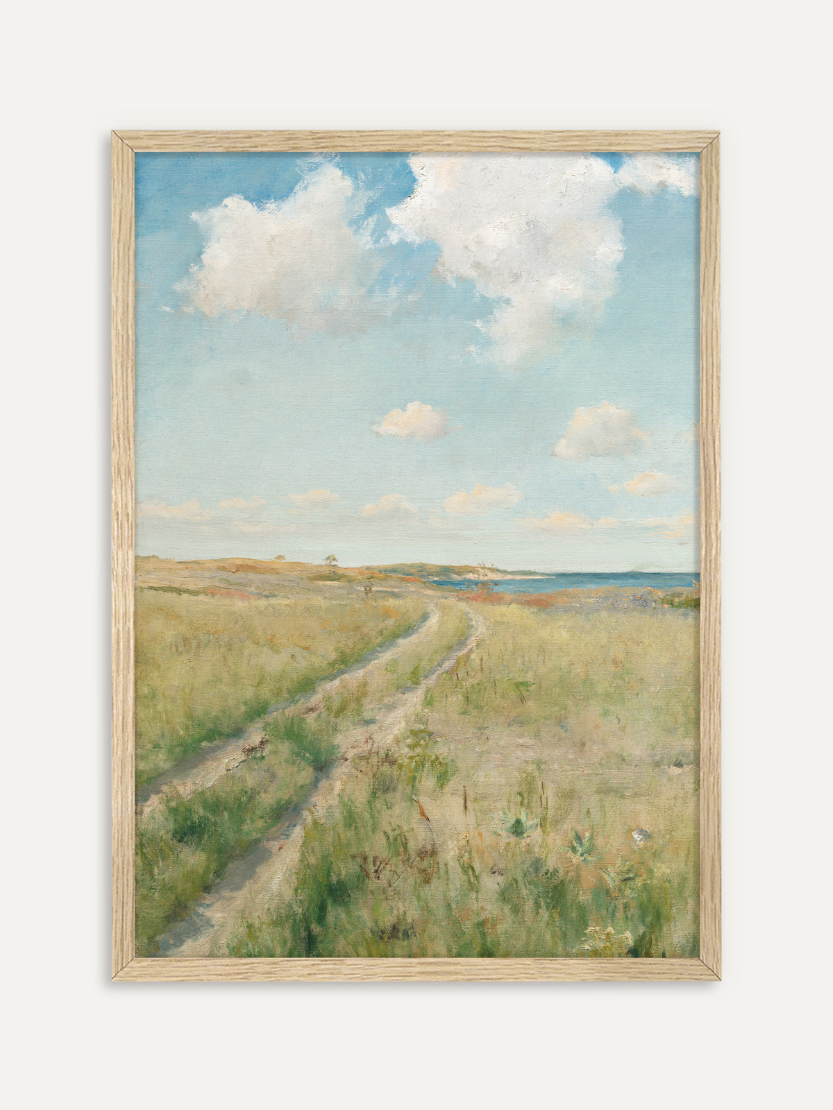 Kunstdruck, der einen sandigen Feldweg zeigt, der sich durch eine grüne Sommerwiese zum blauen Meer zieht, darüber große weiße Wolken an einem hellen Himmel. Der helle Holzrahmen unterstreicht die luftige Japandi Stimmung. #Rahmen_Helles Holz