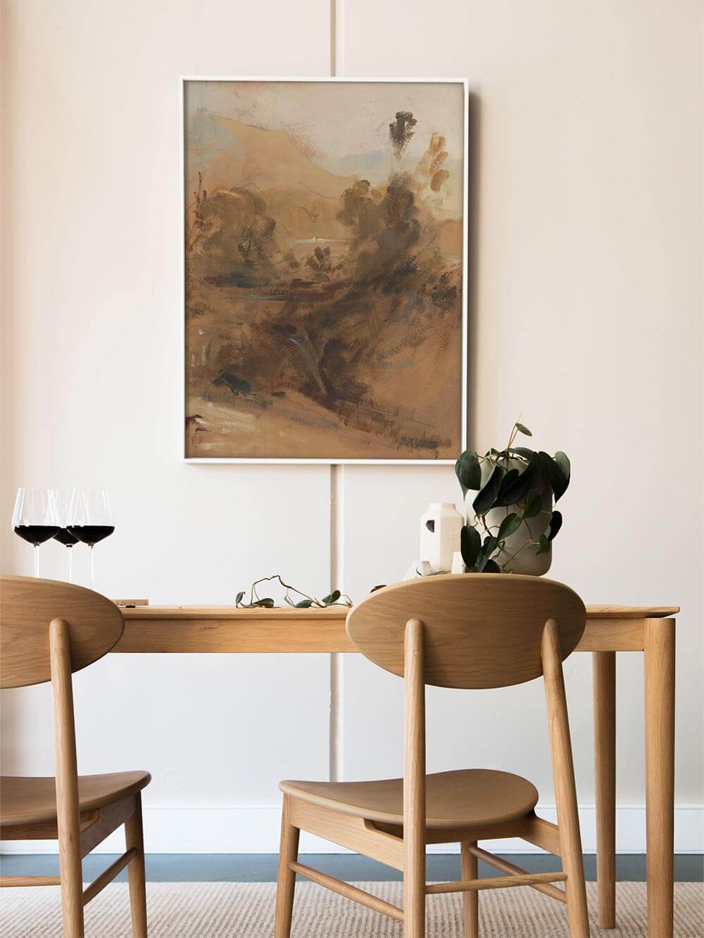 Abstrakter Landschafts-Kunstdruck in erdigen Farben hängt über einem Holztisch im hellen Esszimmer und schafft eine warme, ruhige Atmosphäre. Die organischen Formen und gedämpften Töne ergänzen natürliche Materialien und wirken harmonisch als Wandbild im Wohn- oder Essbereich.