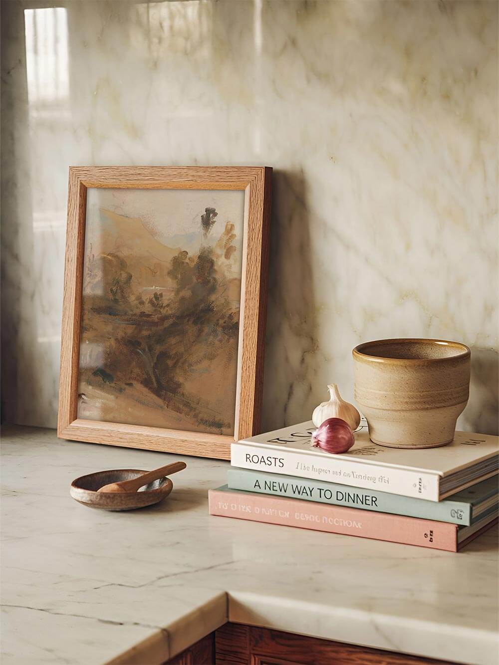 Der abstrakte Landschaftsdruck steht gerahmt auf einer hellen Marmorarbeitsfläche neben Keramik und Kochbüchern und bringt eine ruhige, erdige Note in die Küche. Die malerischen Texturen machen das Poster zu einem dezenten Akzent für natürliche Raumkonzepte.