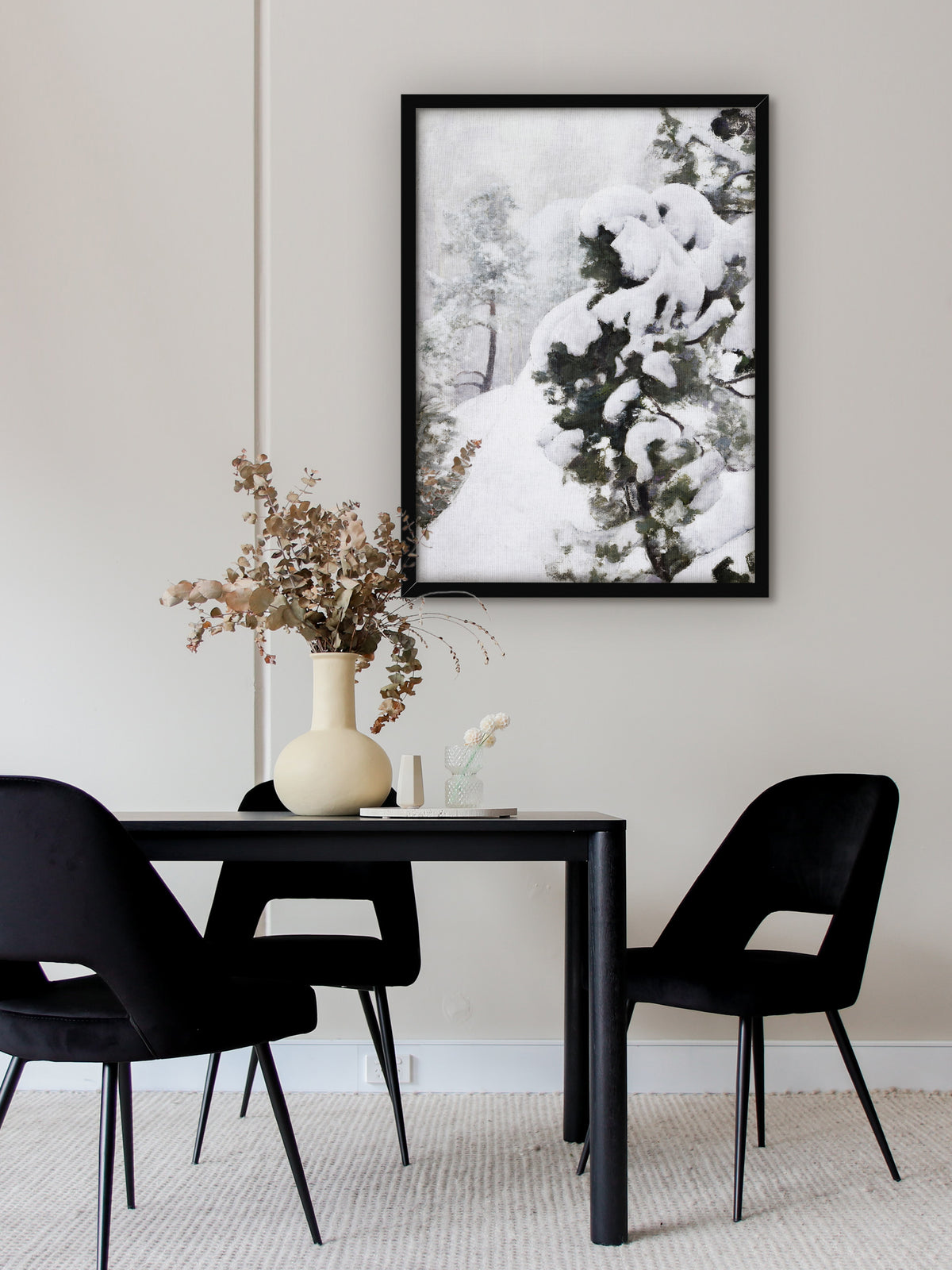 Wabi Sabi Poster einer verschneiten Kiefer im schwarzen Rahmen über einem schwarzen Esstisch mit Samtstühlen und einer Vase mit getrocknetem Eukalyptus. Das Winterbild bringt Ruhe ins moderne Esszimmer.