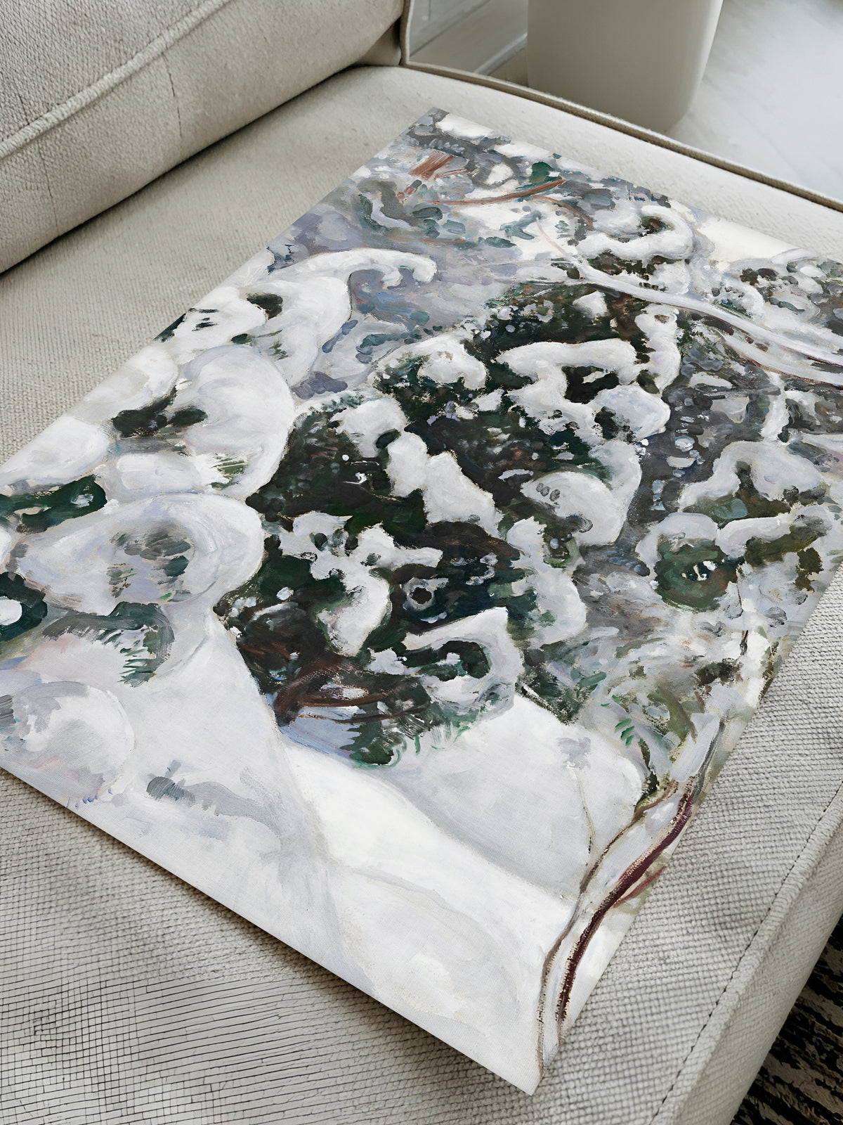 Ungerahmter Kunstdruck eines Wacholders im Schnee, flach auf einem hellen Sofa ausgelegt, sodass die Farben in Weiß, Grau und Grün gut zu sehen sind.
