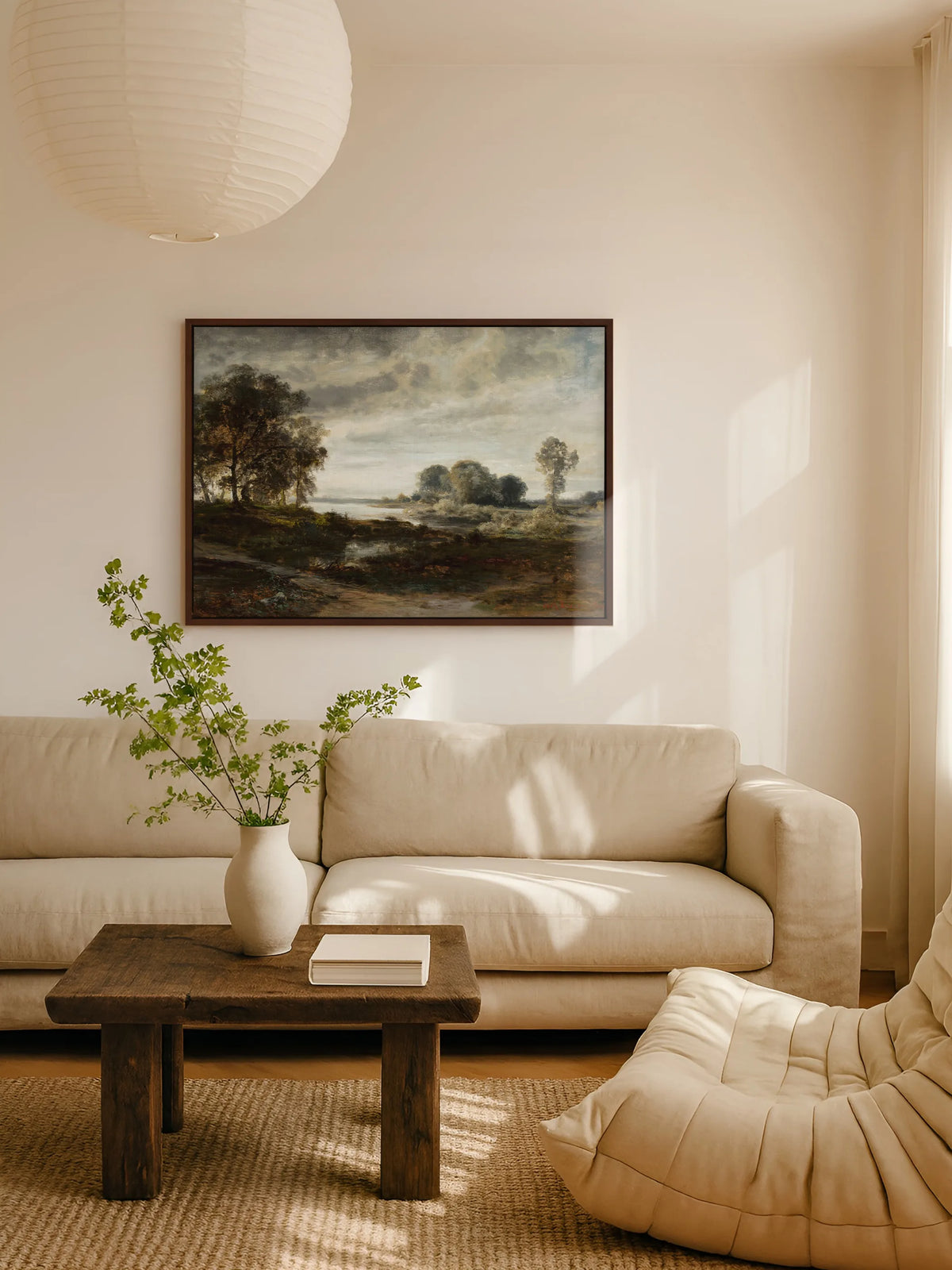 Das Vintage Leinwandbild mit Flusslandschaft hängt im braunen Rahmen über einem beigen Leinensofa im Wohnzimmer. Davor steht ein rustikaler Couchtisch aus dunklem Holz mit einer weißen Vase voller grüner Zweige, darüber eine Papierlampe.