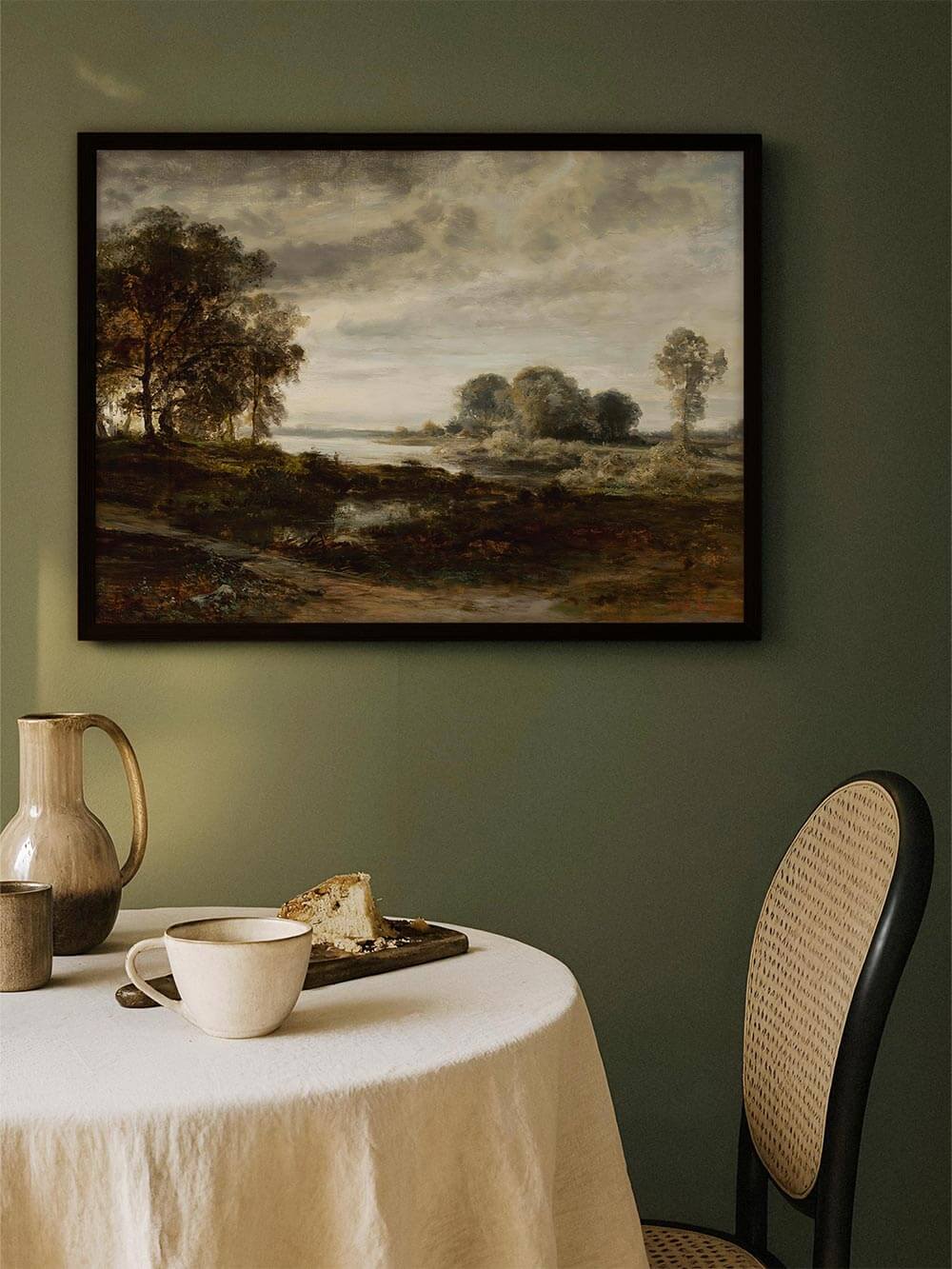 Moody Landschaftskunstdruck in dunklem Rahmen über einem gedeckten Esstisch vor grüner Wand, kombiniert mit Keramik und Leinen. Das Wandbild schafft eine ruhige, elegante Atmosphäre und passt ideal zu natürlicher Raumdekoration.