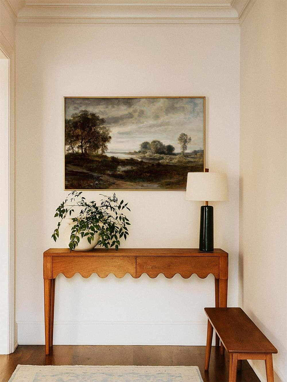 Breitformatiger Landschaftskunstdruck über einer Holzkonsole im hellen Flur, ergänzt durch Pflanze und Tischlampe. Die gedämpfte Farbpalette verleiht dem Raum Tiefe und unterstreicht einen zeitlosen, klassischen Einrichtungsstil.