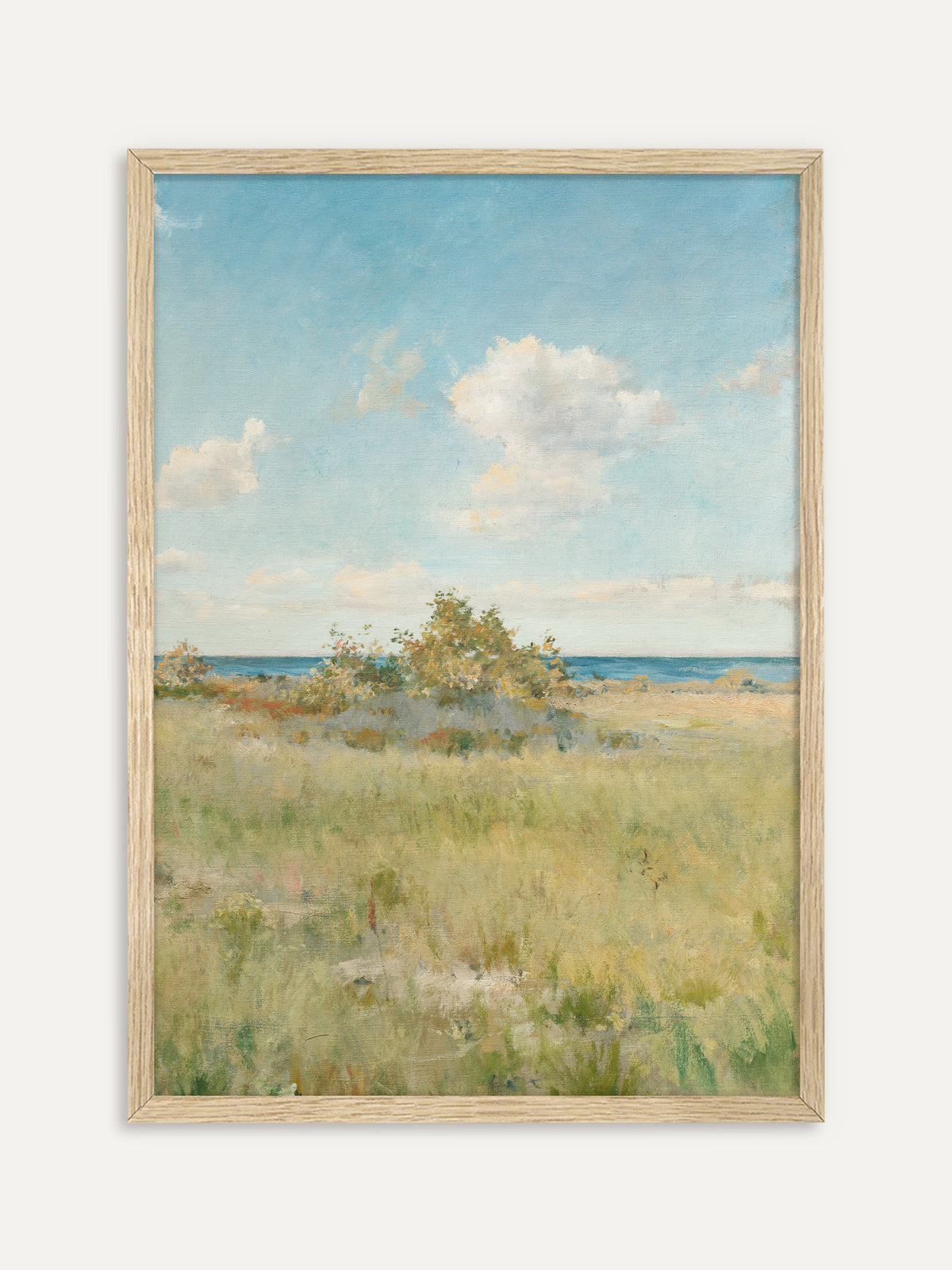 Kunstdruck, der eine goldgrüne Küstenwiese mit einem Gebüsch vor dem blauen Meer zeigt, darüber leichte weiße Wolken an einem hellen Sommerhimmel. Der helle Holzrahmen passt zur natürlichen Wabi-Sabi Stimmung der Wiese. #Rahmen_Helles Holz