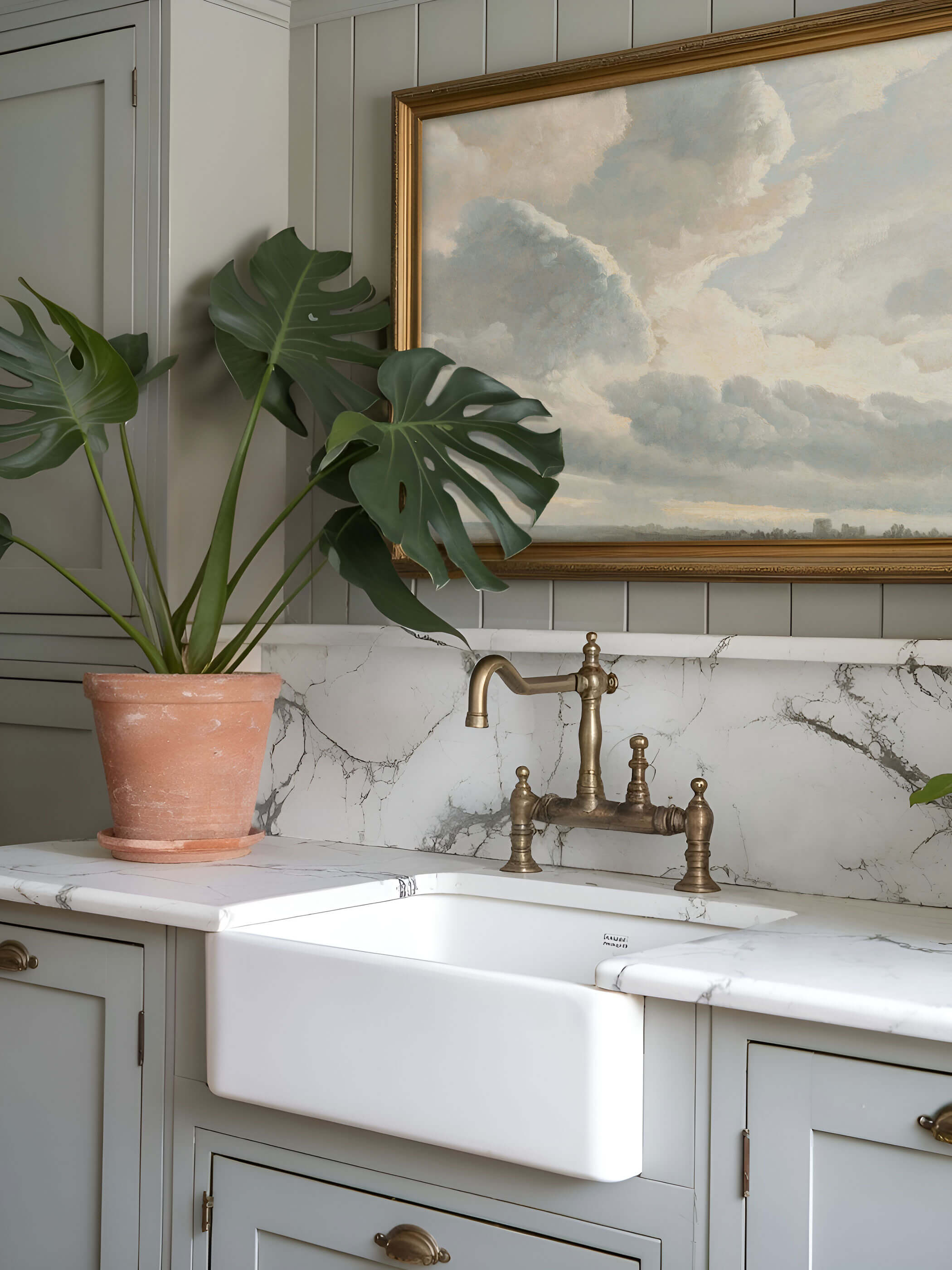 Vintage Wolken-Kunstdruck in einem Landhausstil-Küchenbereich. Der Druck ist in einem goldenen Rahmen über einem eleganten Marmorspülbecken mit Pflanzenarrangement und klassischer Armatur.