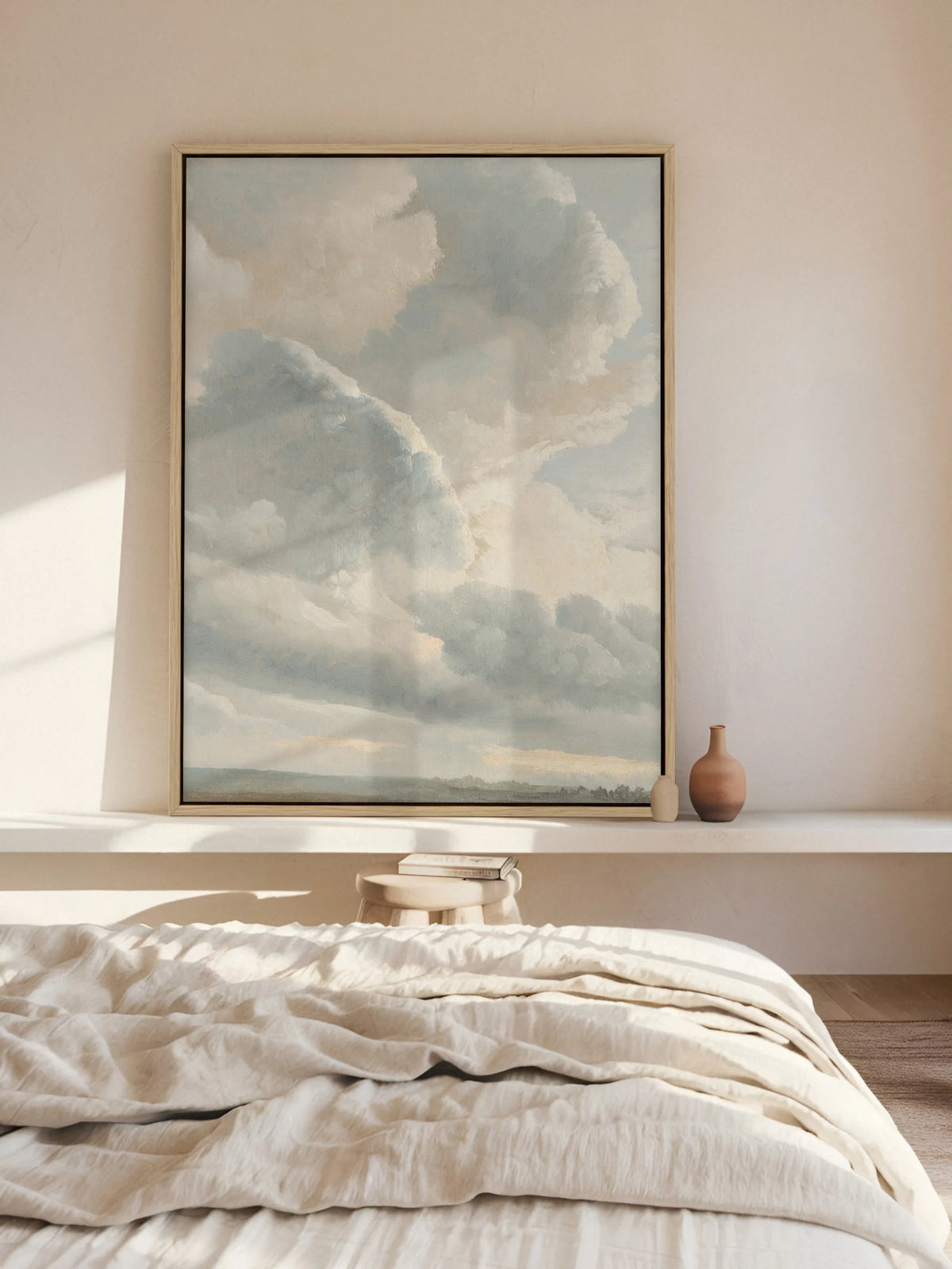 Vintage Wolken Leinwandbild im Naturholzrahmen, angelehnt auf einem weißen Wandbord hinter dem Bett. Daneben stehen zwei kleine Tonvasen, Sonnenlicht fällt über die zerknitterte Leinenbettwäsche und das Bild.
