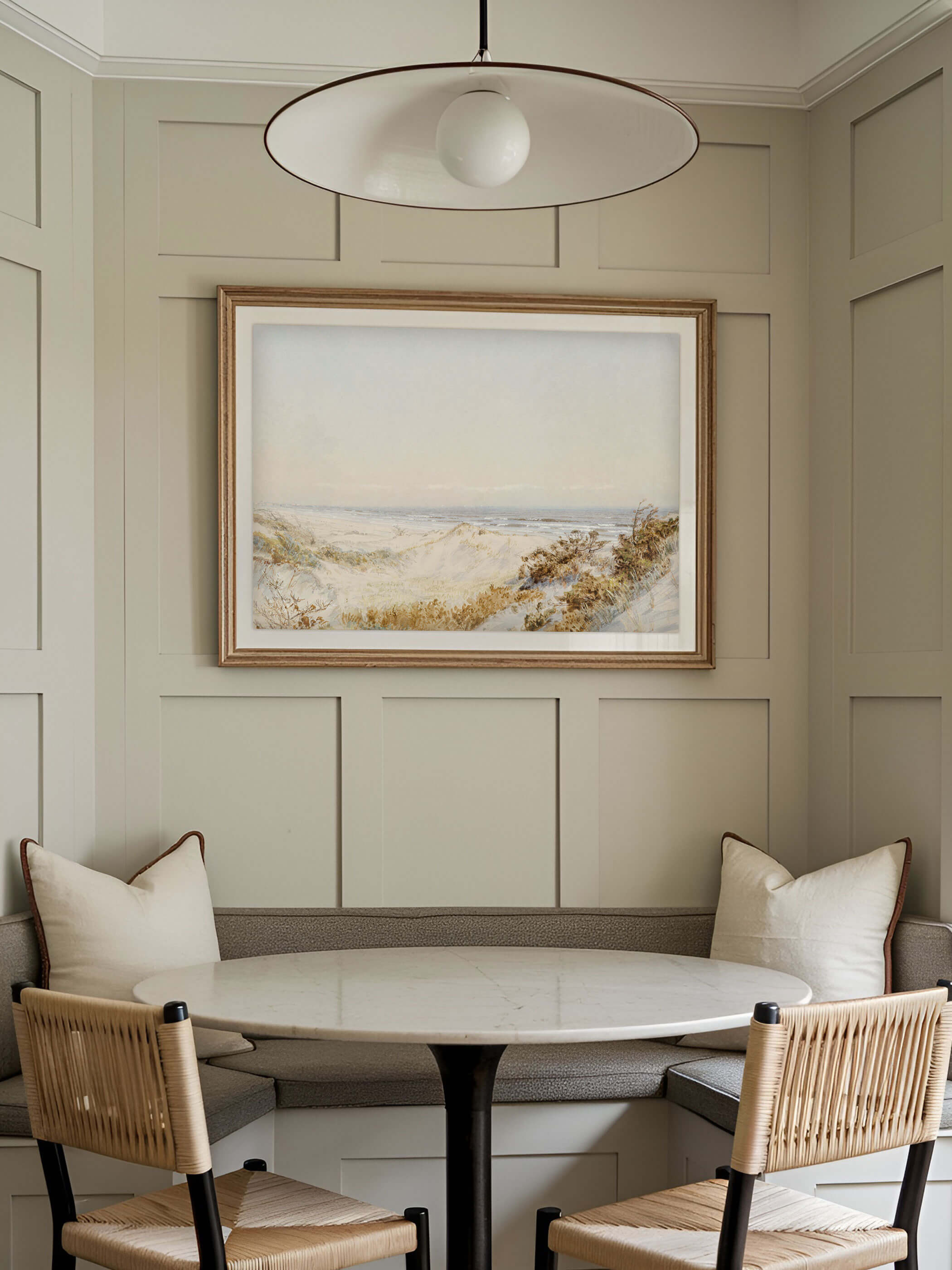 Vintage Kunstdruck von Dünen am Atlantik in einem goldenen Rahmen, elegant präsentiert in einer gemütlichen Ess-Ecke mit Holzmöbeln und Kissen.