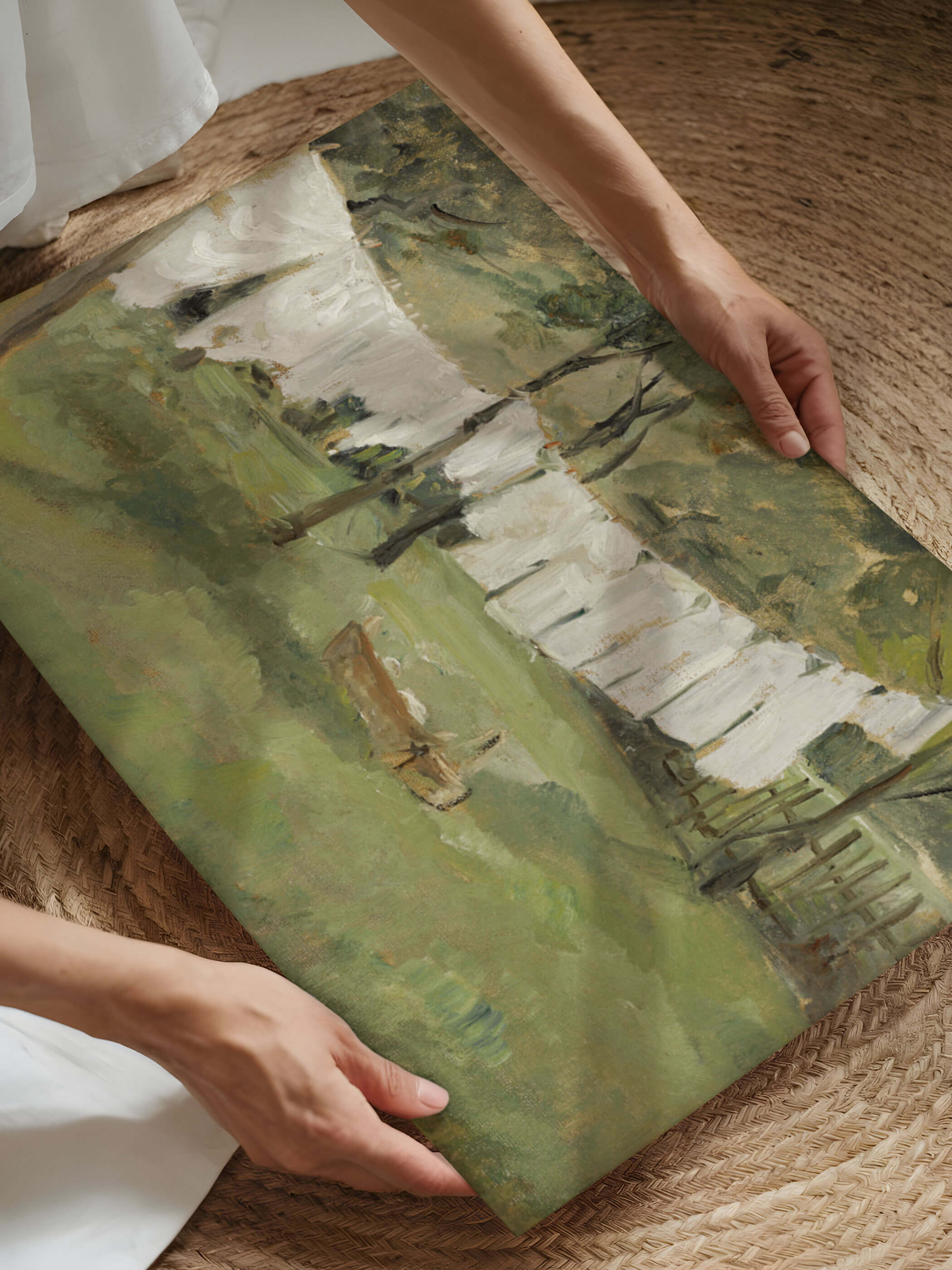 Person hält einen Vintage-Kunstdruck von Johann Sperl, der eine Wäscheleine mit weißen Laken in einer grünen Wiese zeigt. Der Kunstdruck wird auf einem gewebten runden Teppich präsentiert.