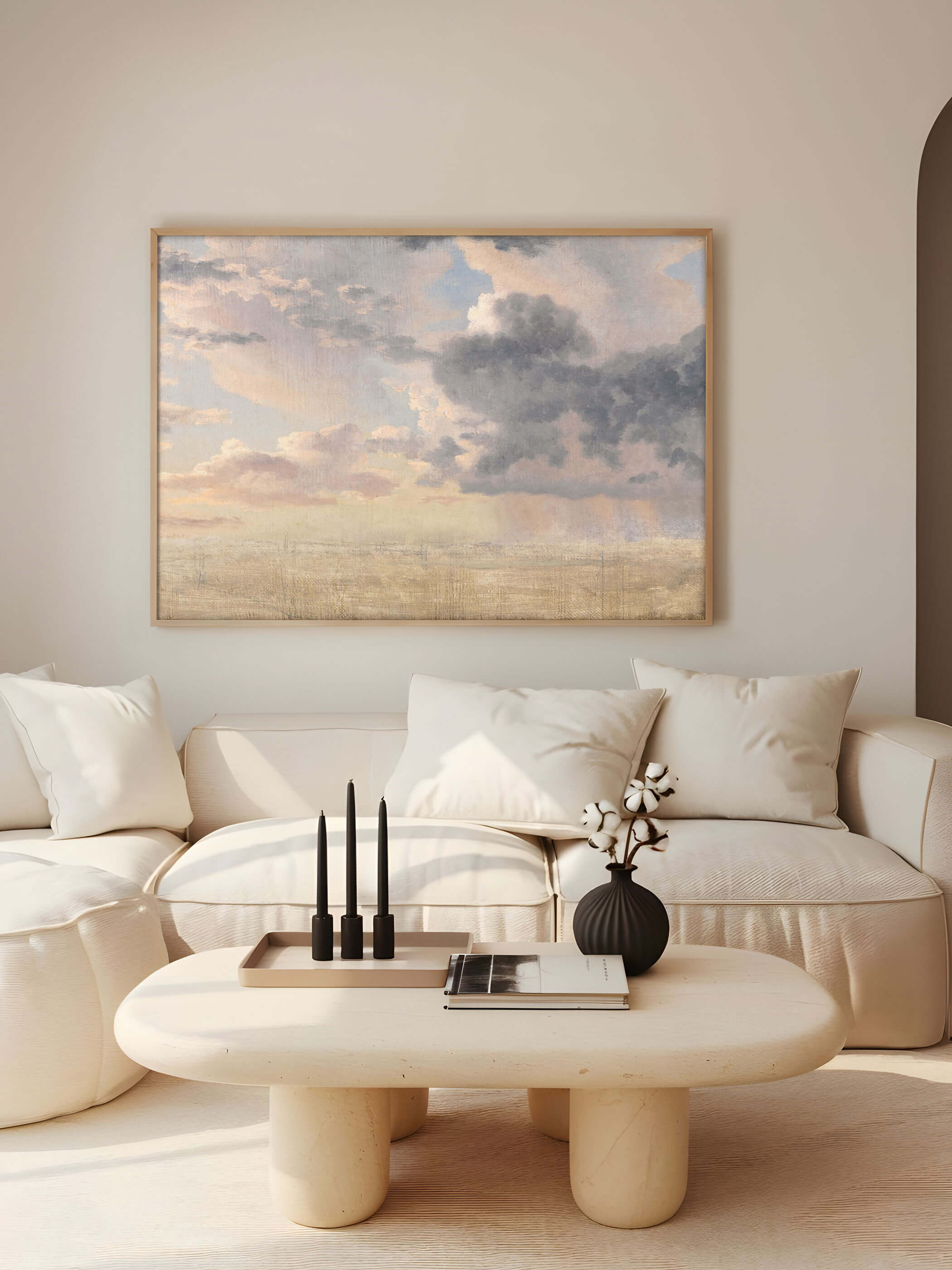 Poster eines dramatischen Wolkenhimmels über einem minimalistischen, beigen Sofa in einem modernen Wohnzimmer mit natürlichem Licht.