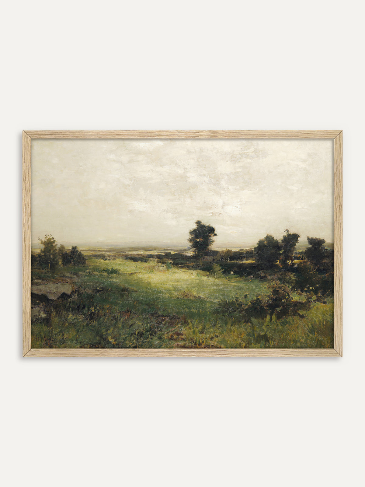 Kunstdruck, der eine weite grüne Wiese mit Felsen und dunklen Baumgruppen zeigt, dahinter ein flaches Tal unter einem hellen, cremeweißen Himmel. Im Rahmen aus hellem Holz wirkt die Vintage-Landschaft ruhig und natürlich. #Rahmen_Helles Holz