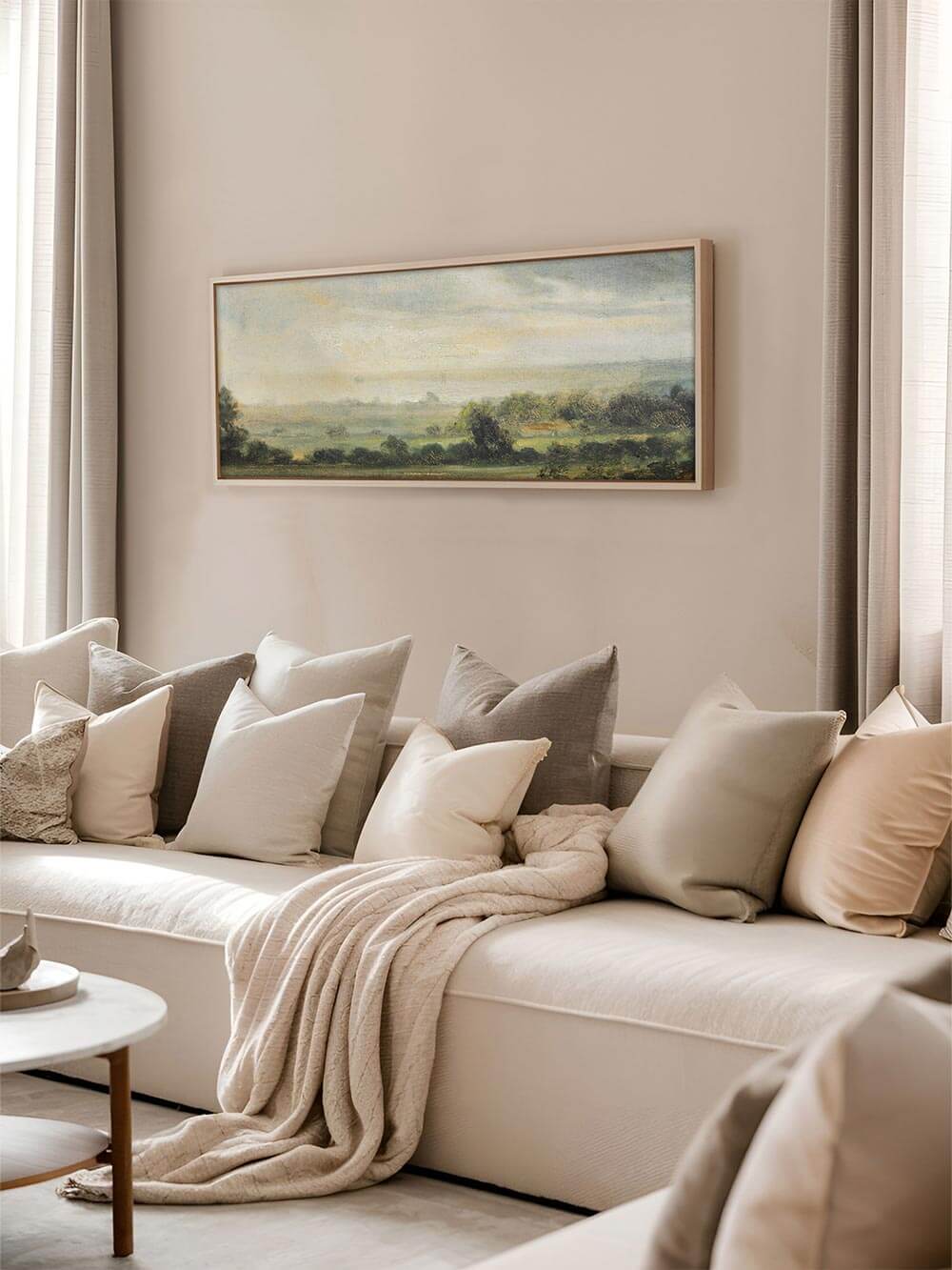 Eleganter Panorama-Landschaftsdruck über einer gemütlichen, neutralen Sofalandschaft, eingerahmt in Naturholz, mit sanften Grüntönen und pastellfarbenem Himmel – harmonische Kunst für moderne Wohnräume.