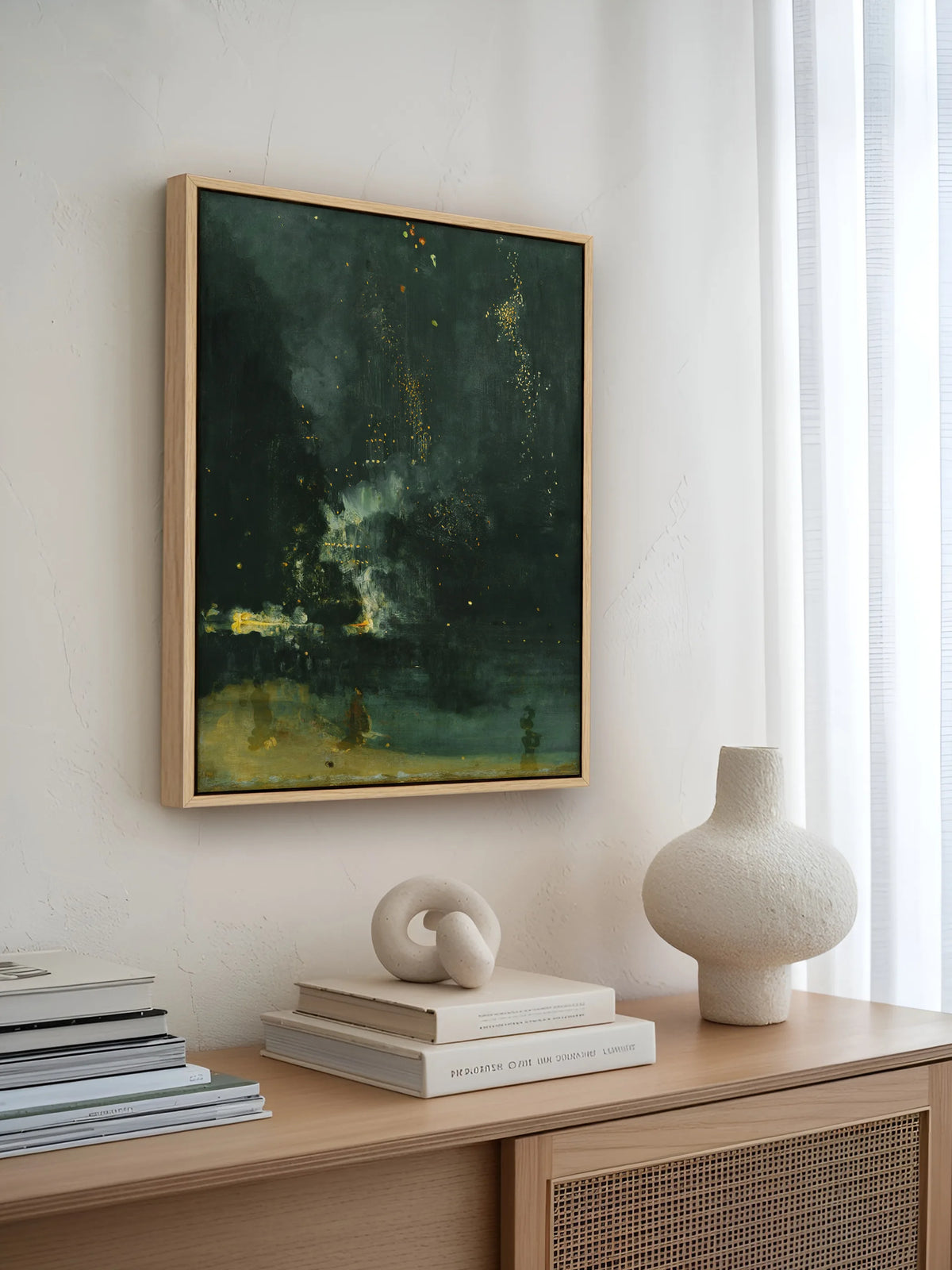 Leinwandbild in Schwarzgrün und Gold im naturfarbenen Rahmen über einem Sideboard mit Rattan, hellen Büchern und Vase aus Keramik