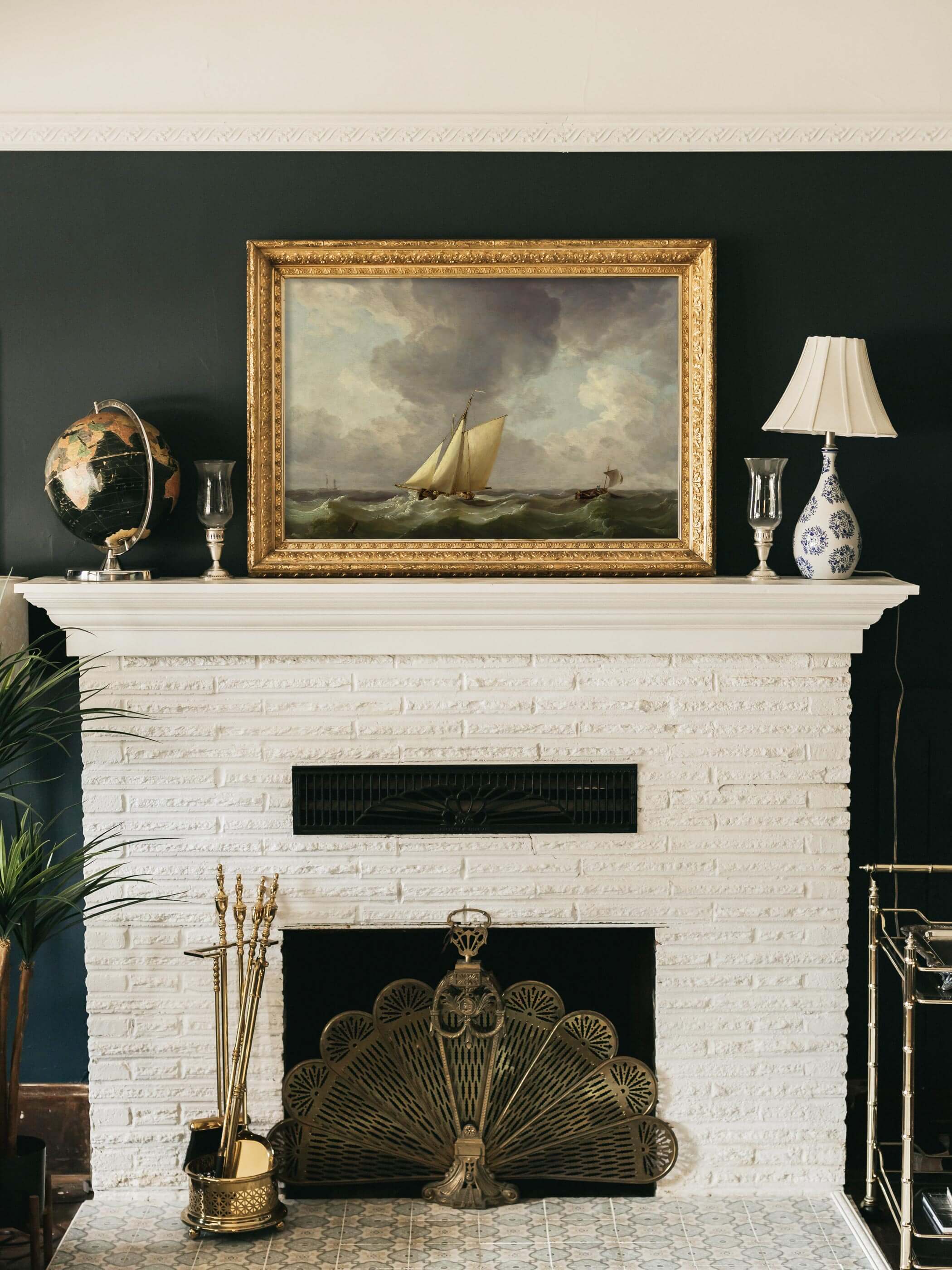 Maritimer Kunstdruck mit Segelbooten auf stürmischer See, stilvoll eingerahmt über einem weißen Kamin mit goldenen Akzenten und einem Globus im Wohnzimmer.