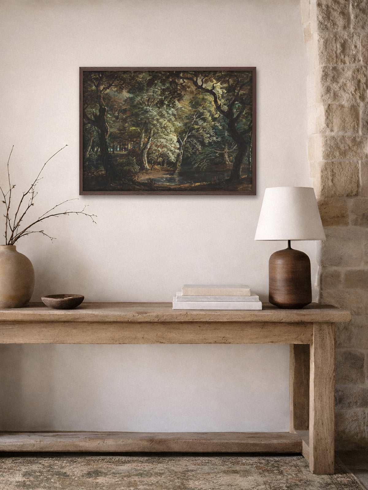 Waldlandschaft mit Teich als Kunstdruck im dunklen Holzrahmen über einer rustikalen Holzkonsole mit Tonvase, Holzschale und Tischlampe neben einer Natursteinwand.