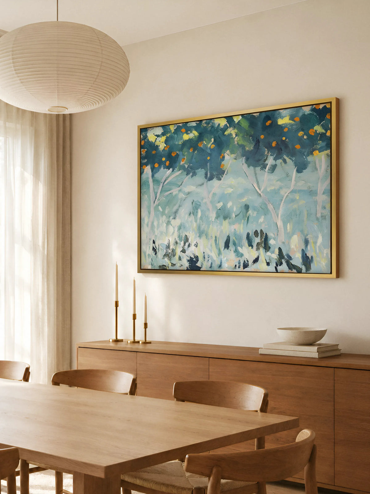 Großes Impressionismus Leinwandbild mit Orangenhain im goldenen Rahmen über einem Sideboard aus warmem Holz im Esszimmer. Darauf stehen drei Messingleuchter mit Kerzen und eine Steinschale, davor ein Holztisch mit Stühlen.