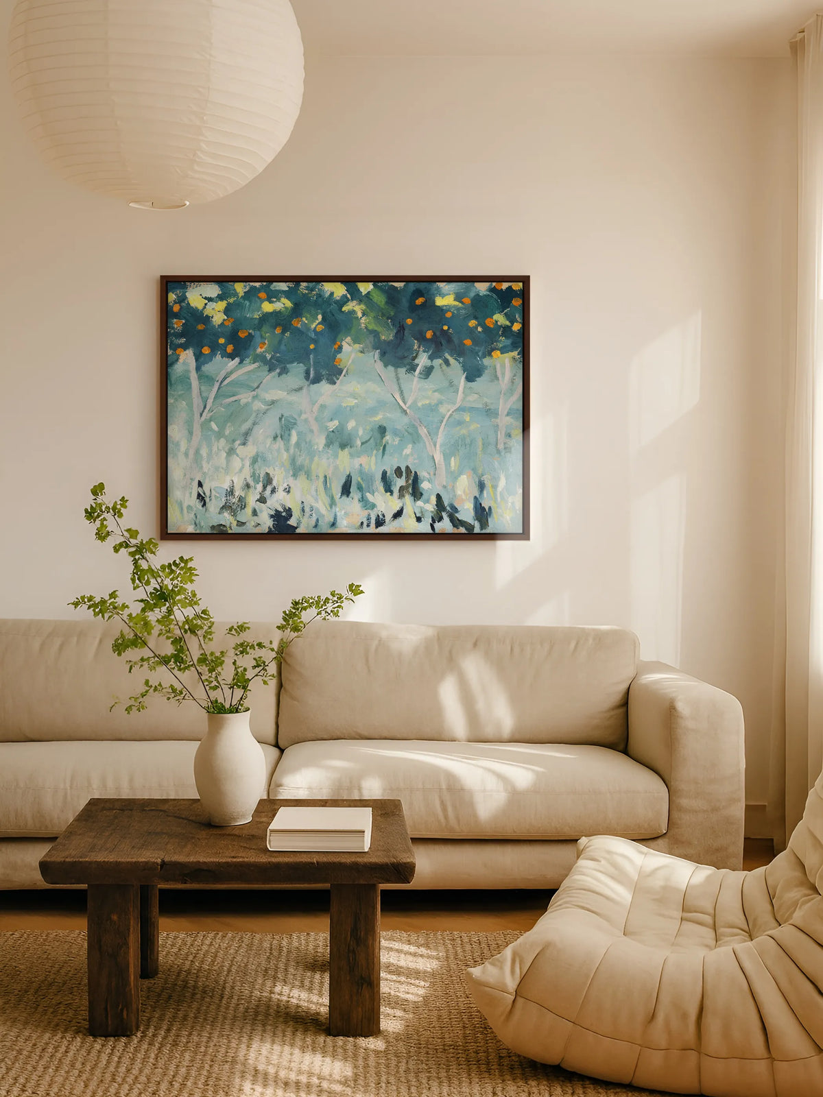 Das Leinwandbild mit Orangenbäumen hängt im braunen Rahmen über einem beigen Leinensofa im Wohnzimmer. Davor steht ein rustikaler Couchtisch aus dunklem Holz mit einer weißen Vase voller grüner Zweige, darüber eine Papierlampe.