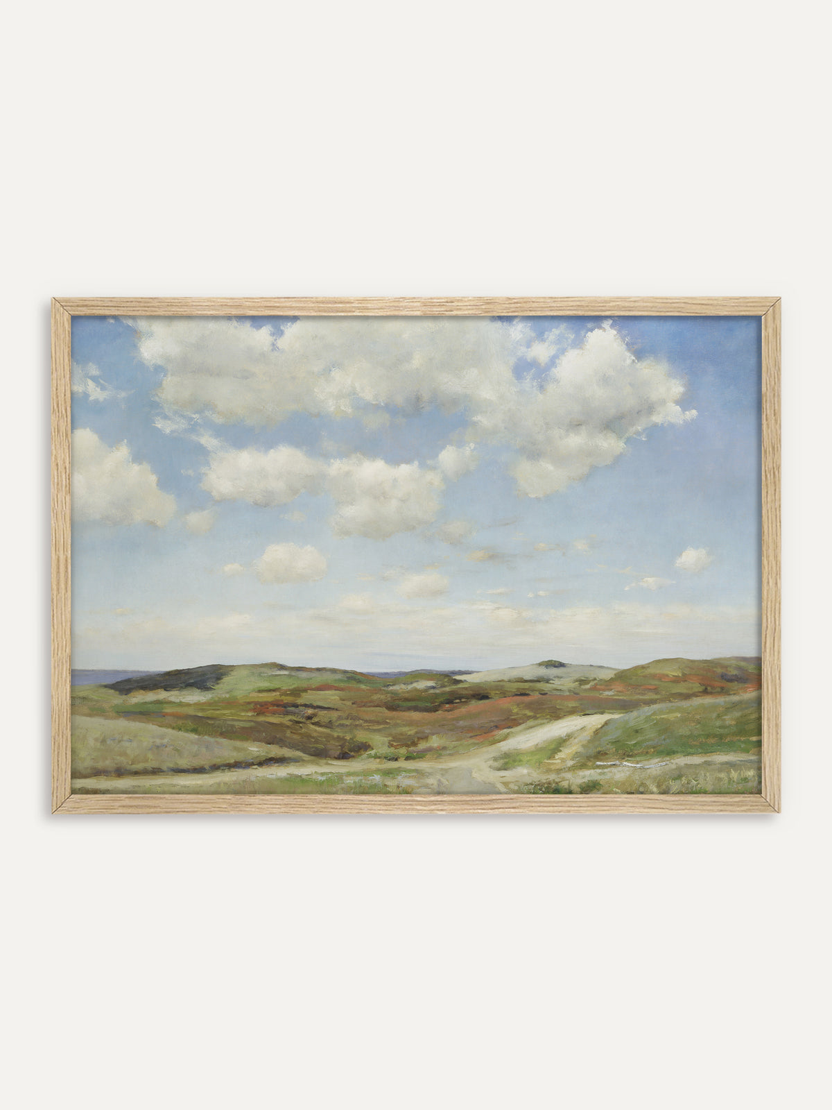 Kunstdruck, der eine Dünenlandschaft mit weißen Sommerwolken über sandigen Hügeln zeigt, bewachsen mit Heide in Grün und Rostrot, durch die ein heller Weg zum Meer führt. Im Rahmen aus hellem Holz wirkt die Küstenlandschaft luftig und passt zum skandinavischen Wohnstil. #Rahmen_Helles Holz