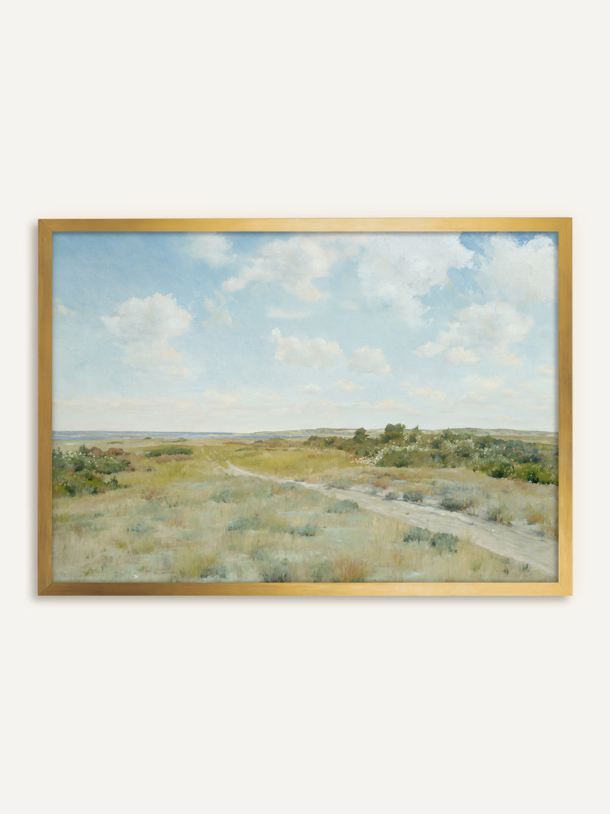 Wandbild, das eine Heidelandschaft mit einem sandigen Weg durch salbeigrünes Gras und blühende Büsche zeigt, am Horizont blaues Wasser unter weißen Wolken. Im goldenen Rahmen nimmt das Bild die Ockertöne im Gras auf und wirkt wie ein antikes Gemälde. #Rahmen_Gold