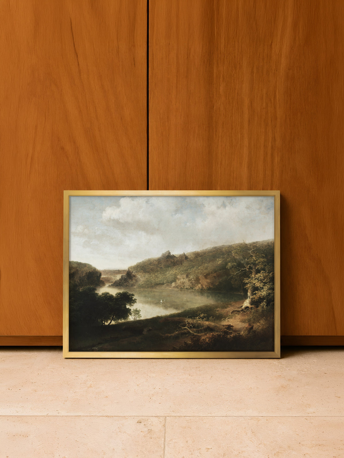 Poster einer Seelandschaft im goldenen Rahmen, angelehnt an eine Wand aus warmem Holz auf einem hellen Steinboden. Das Gold greift das herbstliche Laub im Bild auf.