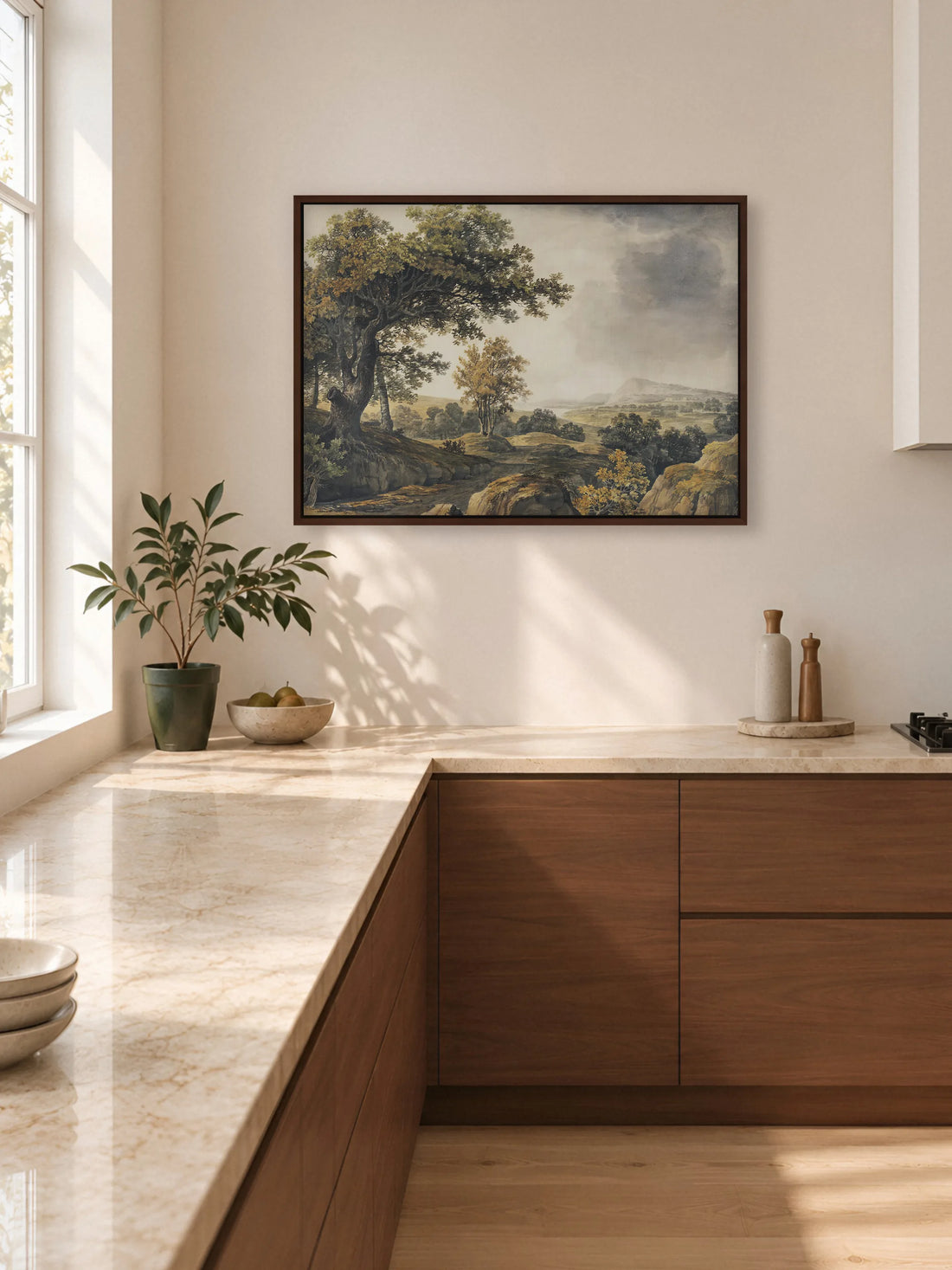 Herbstliche Landschaft als Leinwandbild im braunen Rahmen an einer hellen Küchenwand über einer Arbeitsplatte aus beigem Stein. Darunter stehen Unterschränke aus Nussbaum, eine Pflanze im grünen Topf und eine Schale mit Birnen.